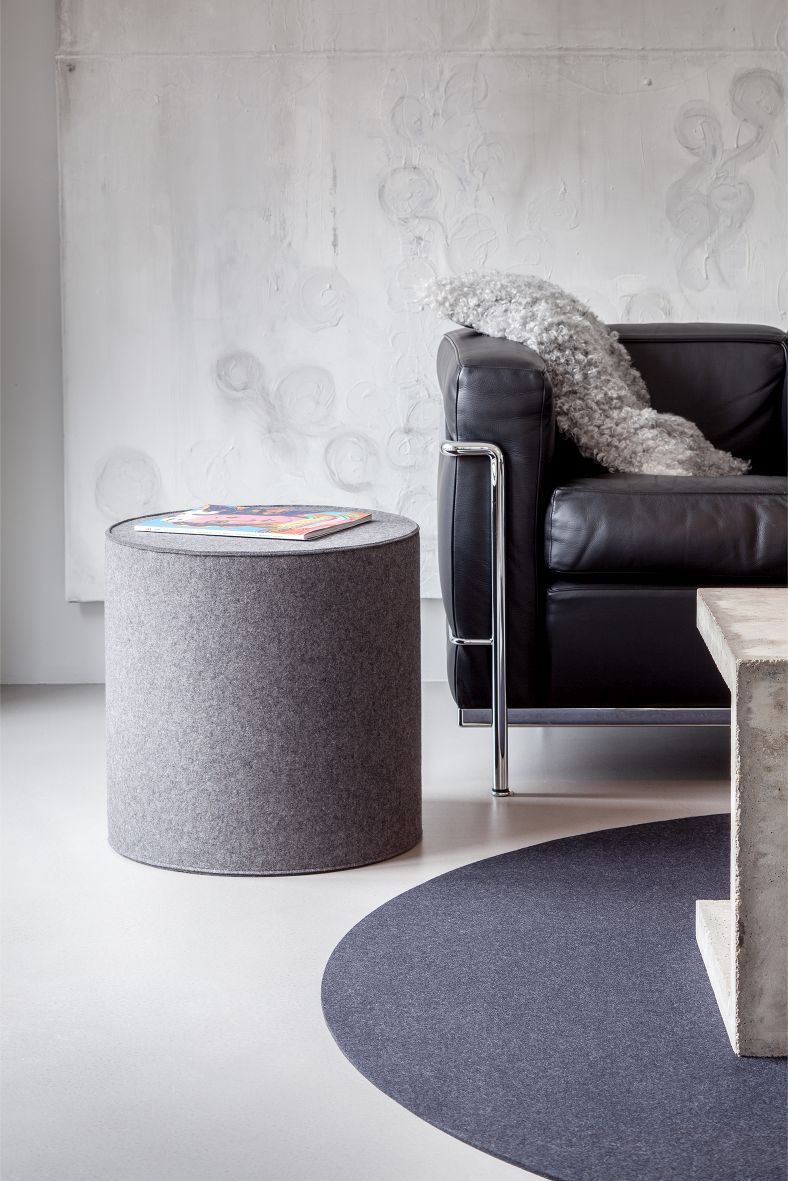 Grauer Bigdot Teppich von HEY-SIGN neben schwarzem Ledersofa und Filzhocker in modernem Wohnzimmer.