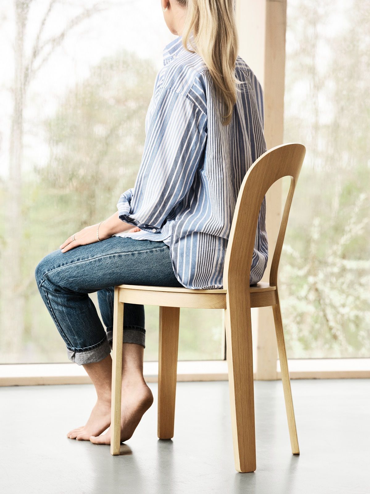 Frau sitzt auf dem Olivia Chair Holzstuhl von Design House Stockholm am Fenster.