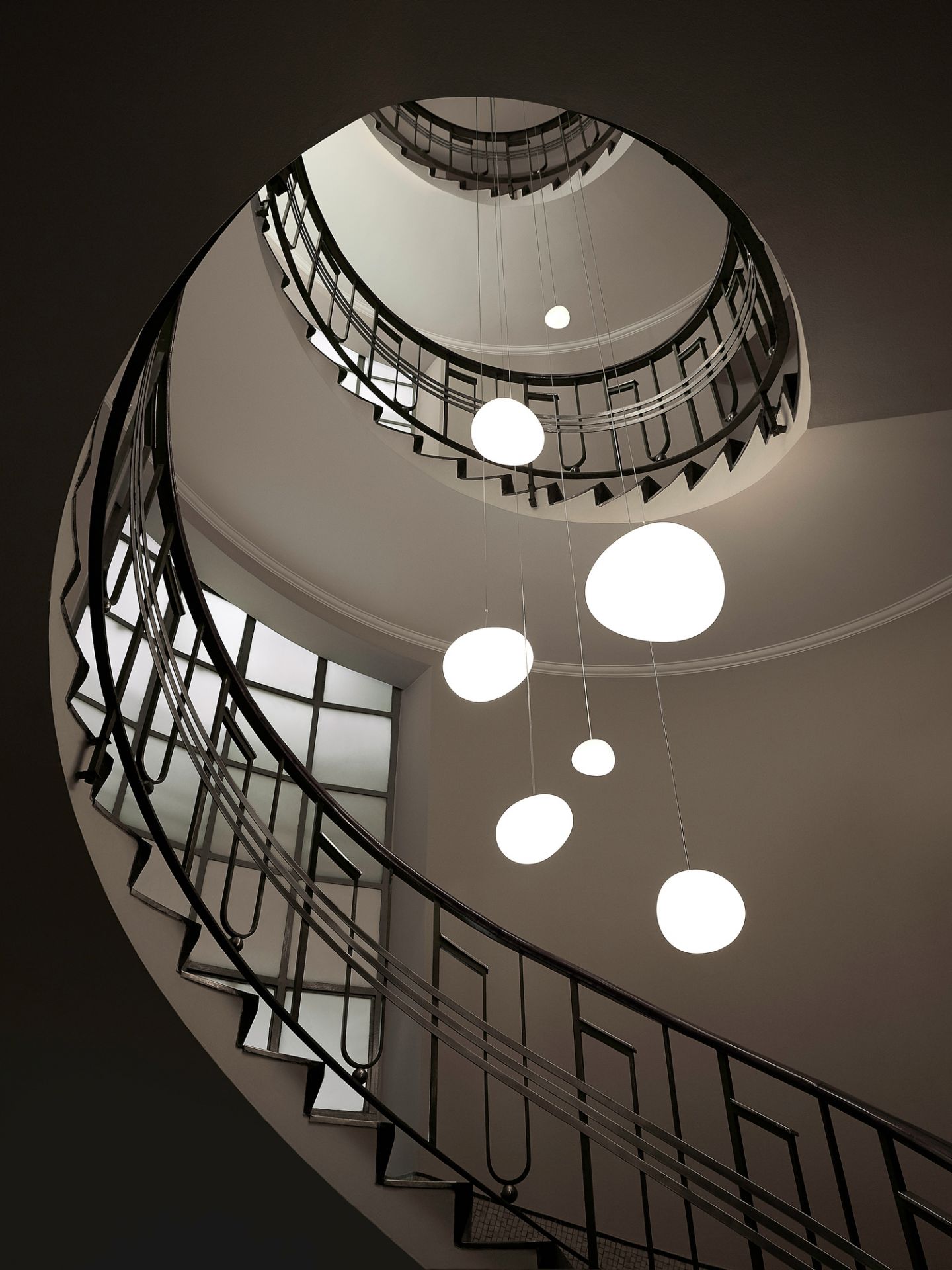 Gregg Pendelleuchte von Foscarini über einer Wendeltreppe, die von oben fotografiert wurde, mit mehreren runden Lampen.