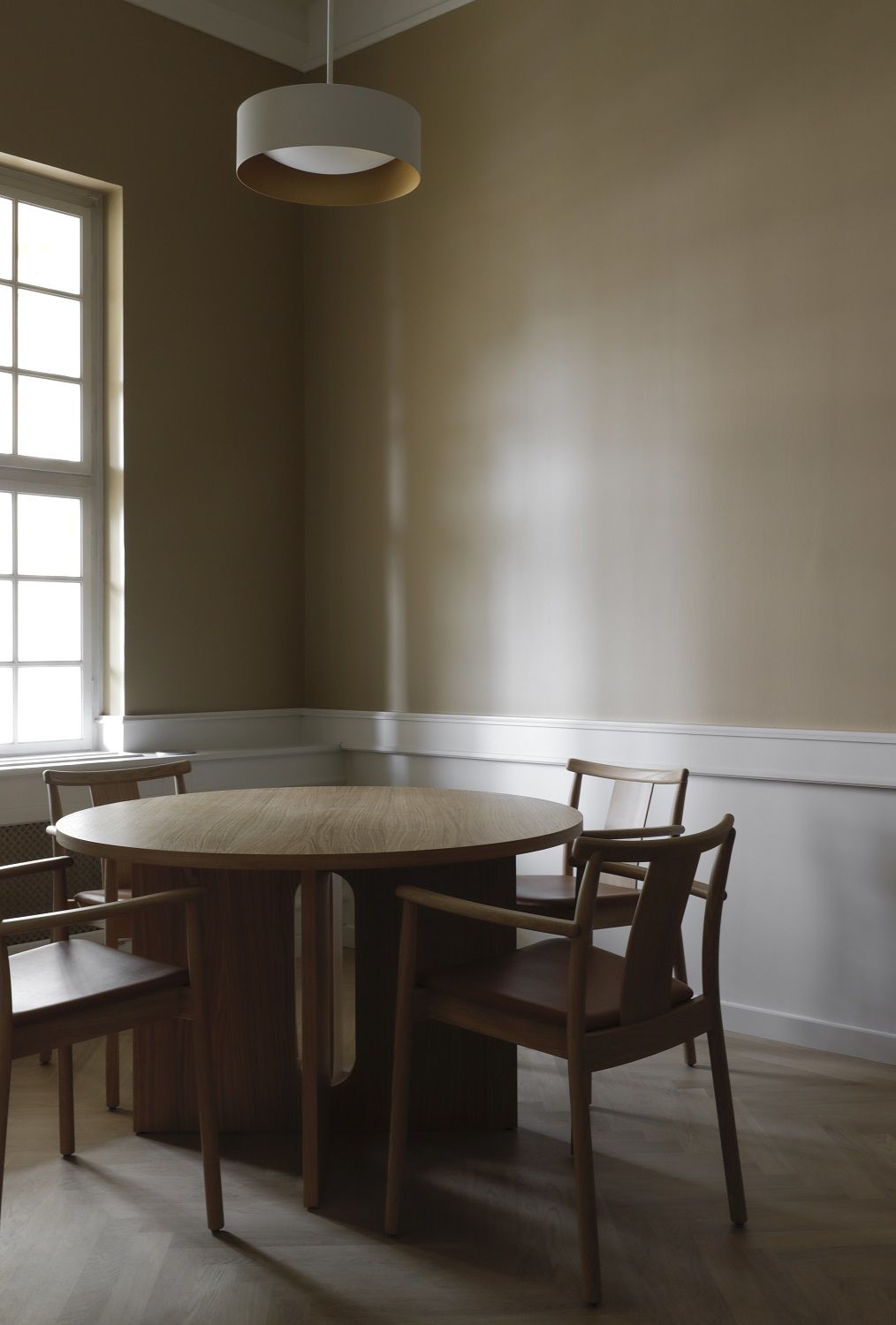 Audo Copenhagen Merkur Dining Chair Stuhl mit Armlehnen an rundem Esstisch aus Holz.