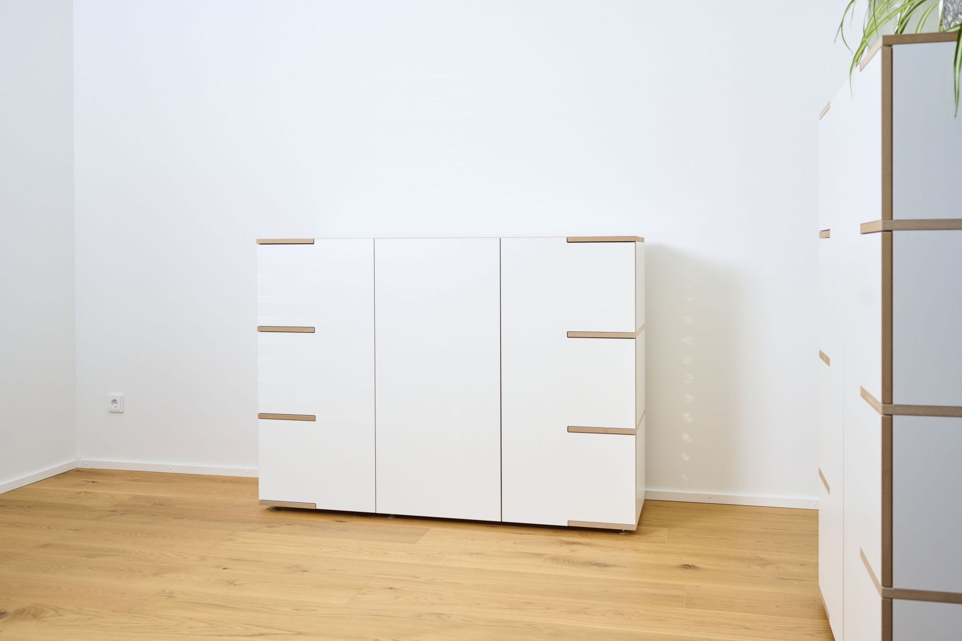 Tojo Stau Sideboard aus weißem Holz mit drei Türen und hellen Holzdetails auf Holzboden.