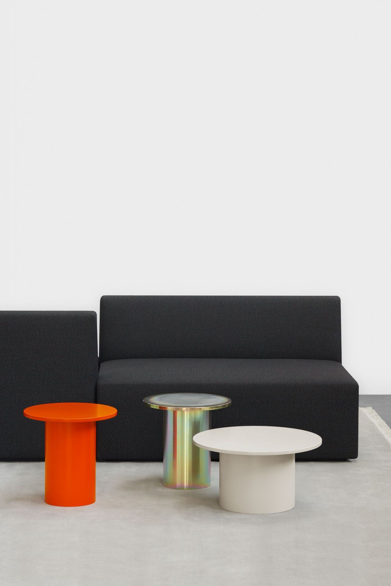 Enoki Beistelltische von e15 in Orange, Beige und irisierend vor einem schwarzen Sofa.