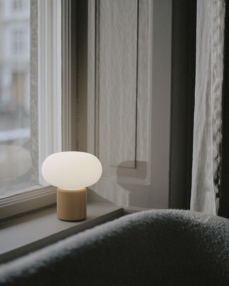 New Works Karl-Johan Tischleuchte, Akkuleuchte in Beige auf einer Fensterbank, warmes Licht.