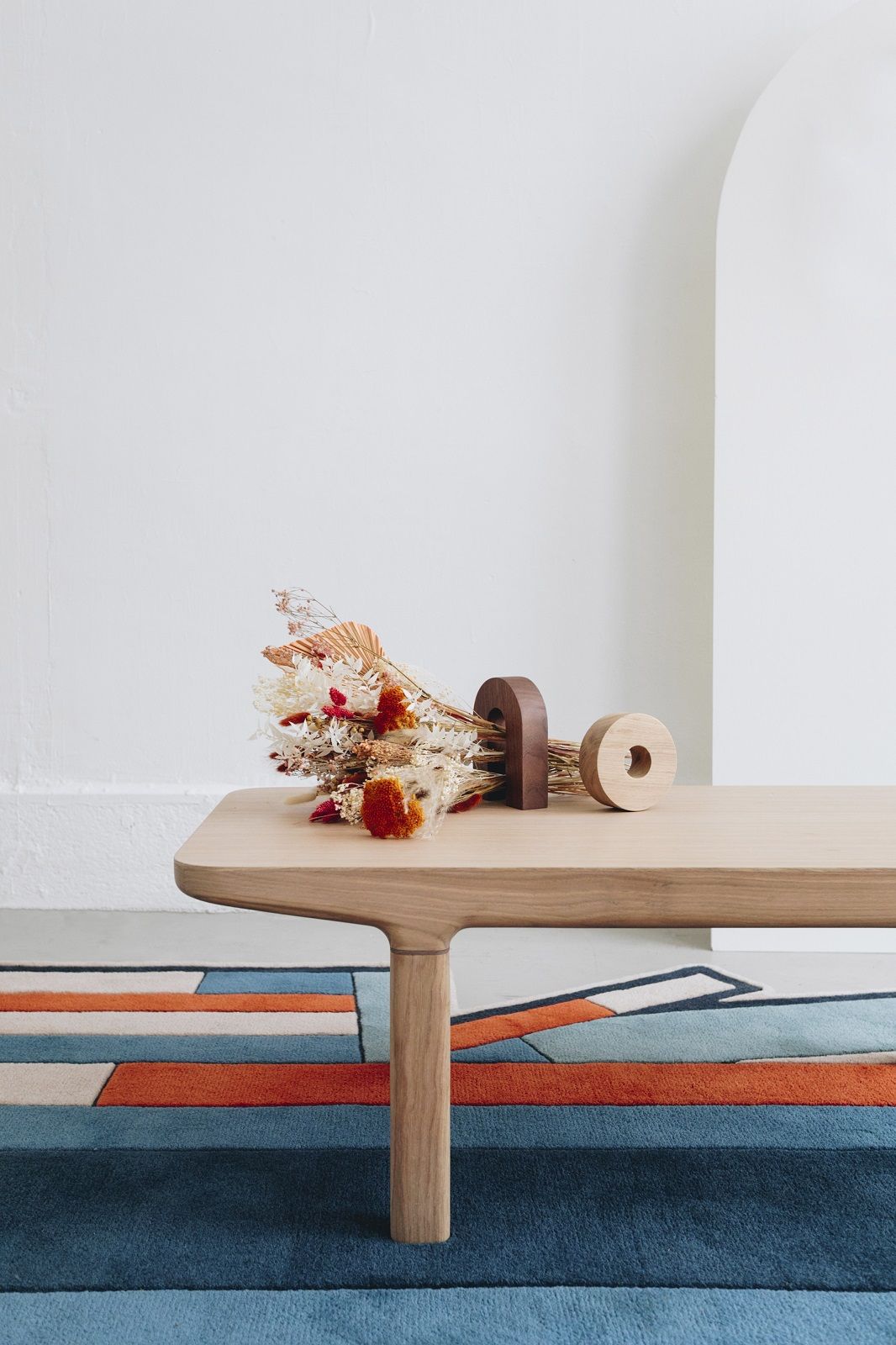 Camille Couchtisch aus Holz mit Trockenblumen und abstrakter Dekoration auf buntem Teppich.