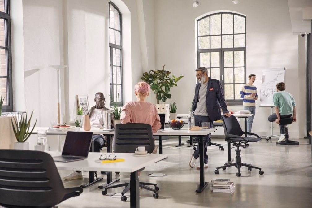 Helles Büro mit Mitarbeitern und einem schwarzen Numo Task Bürodrehstuhl mit Rollen von Aeris im Vordergrund.