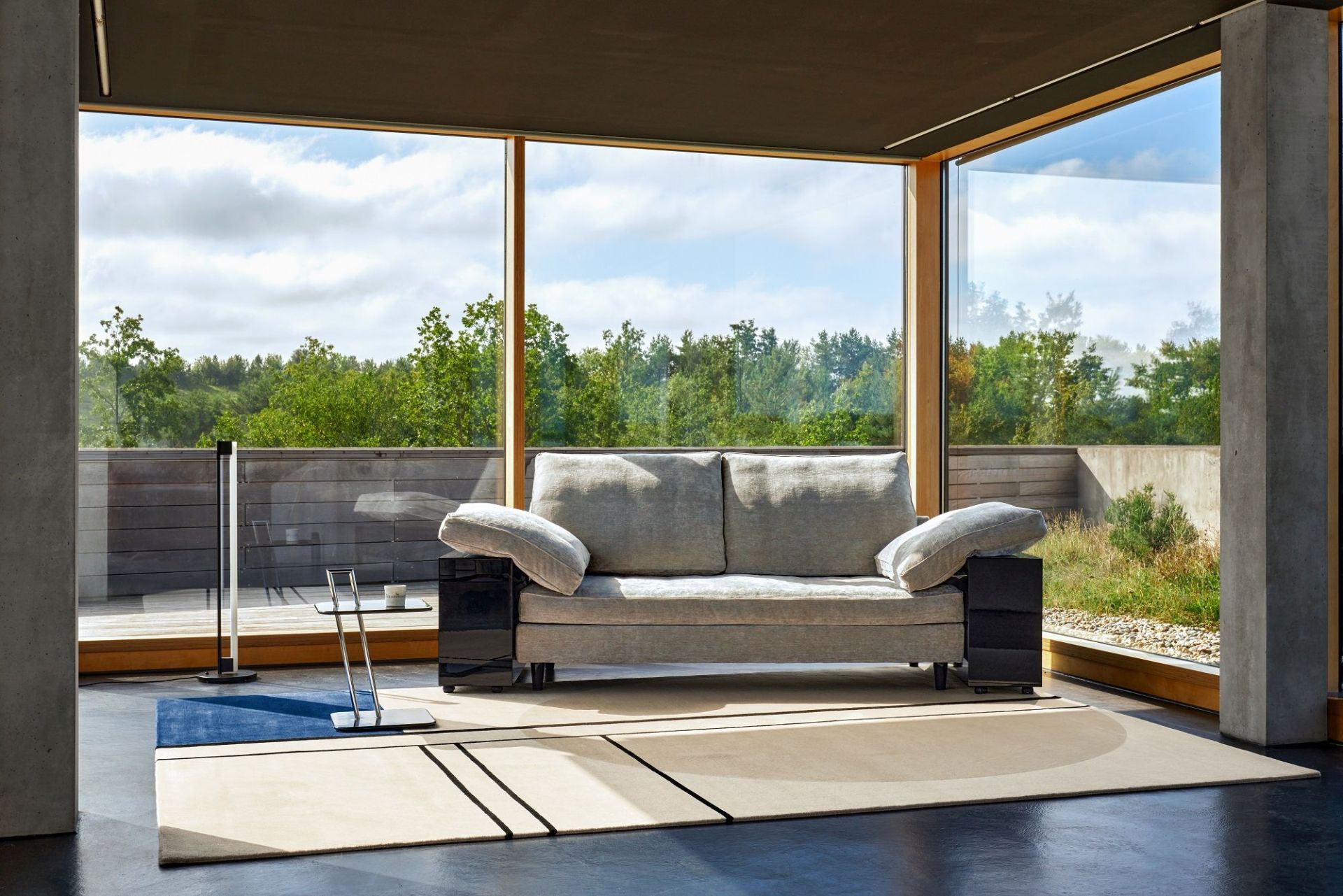 Graues Lota Sofa von Classicon in modernem Wohnzimmer mit großem Fenster und Teppich.