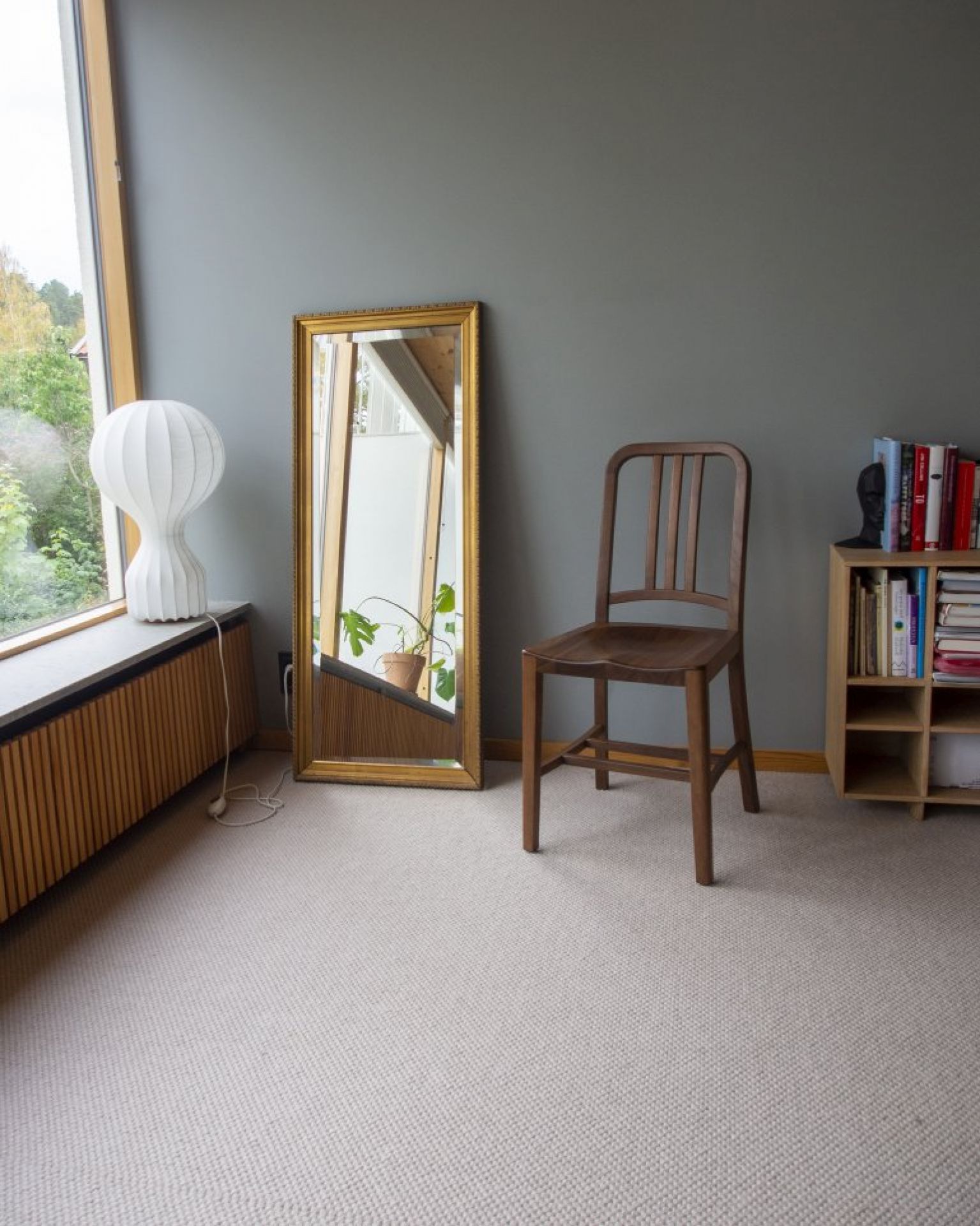 Walnussfarbener Holzstuhl im Raum, möglicherweise ein Navy Wood Chair, neben Spiegel und Bücherregal.