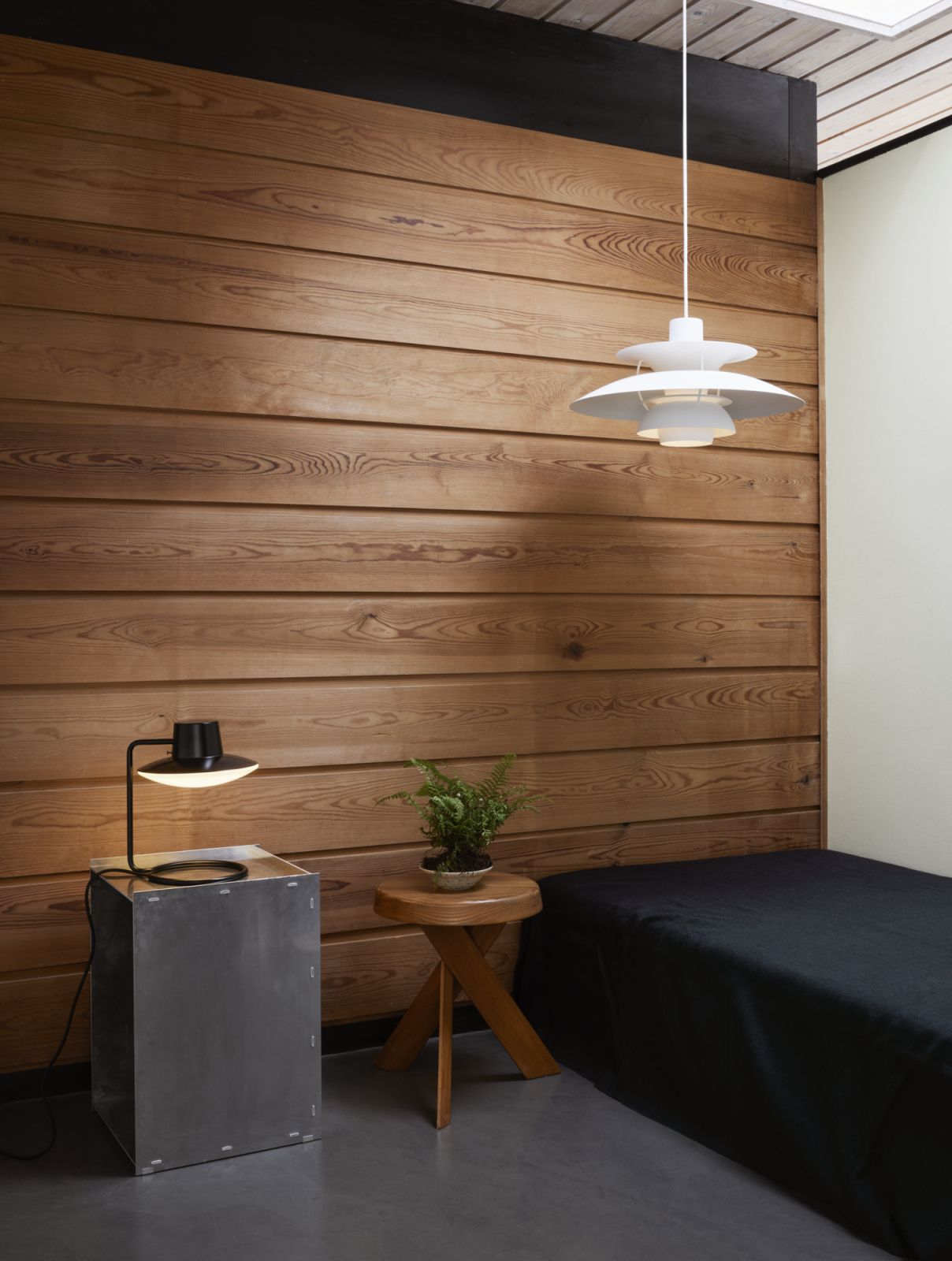 Weiße PH 5 Pendelleuchte von Louis Poulsen hängt über einem Bett vor einer Holzwand.