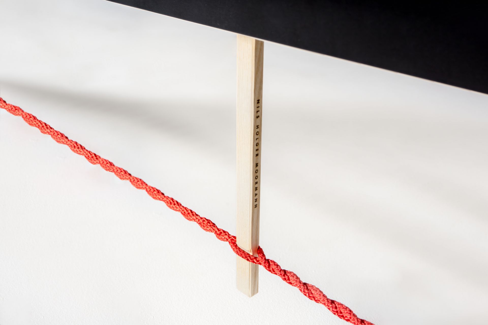 Detailaufnahme der Moormann Langer Max Sitzbank: Rote Kordel, helle Holzstütze mit Logo, minimalistisches Design.
