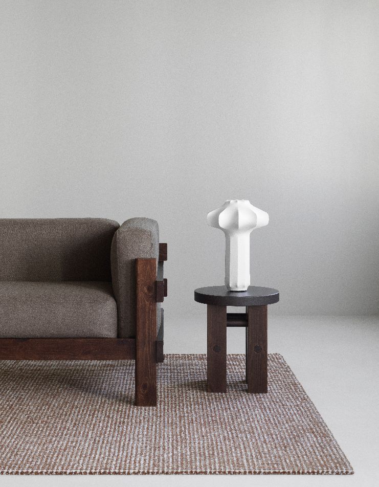 Weiße Phantom Tischleuchte von Normann Copenhagen auf kleinem Holztisch neben Sofa.