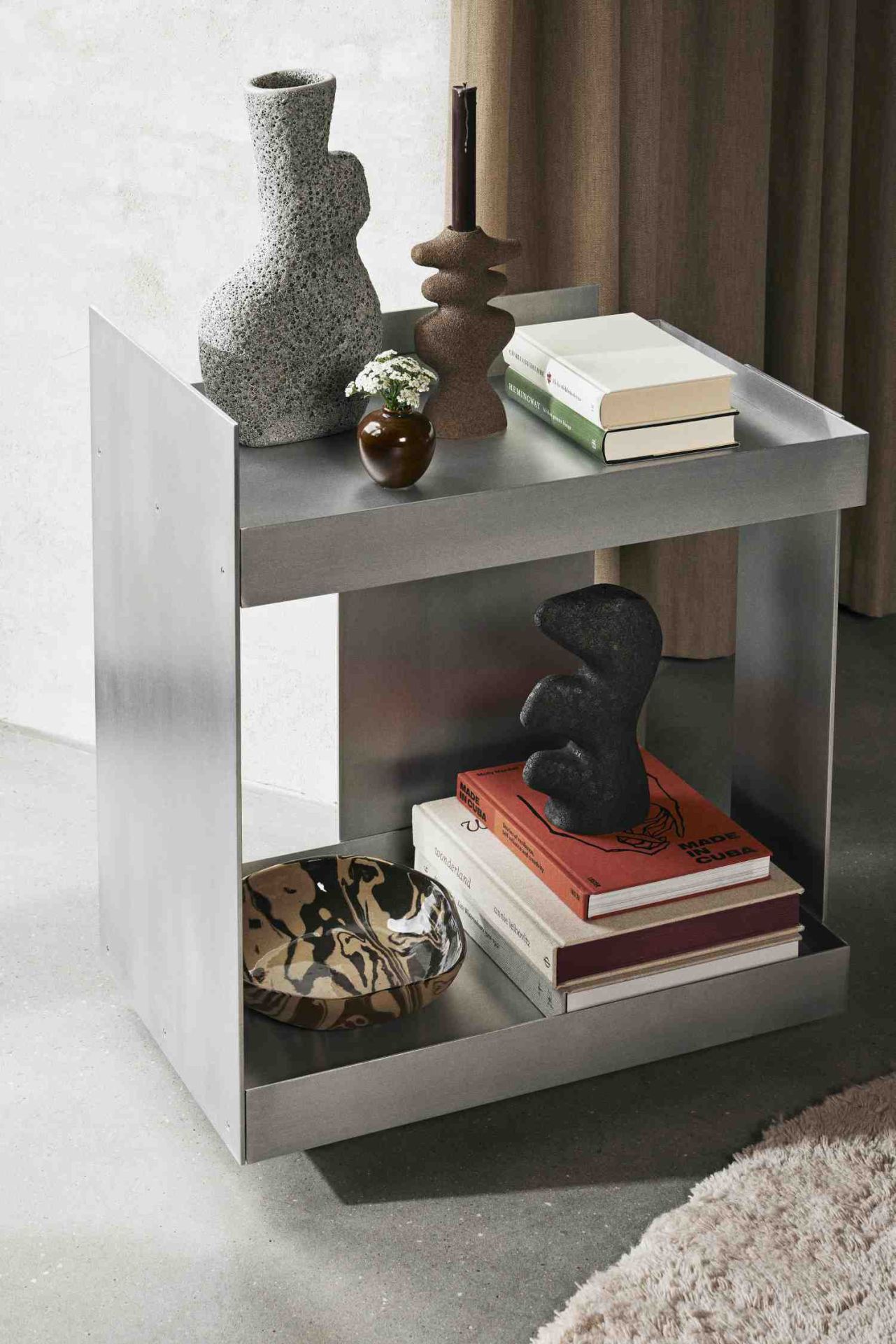 Ferm Living Lager Trolley aus Aluminium, Servierwagen mit zwei Ablageflächen, dekoriert mit Vasen und Büchern.