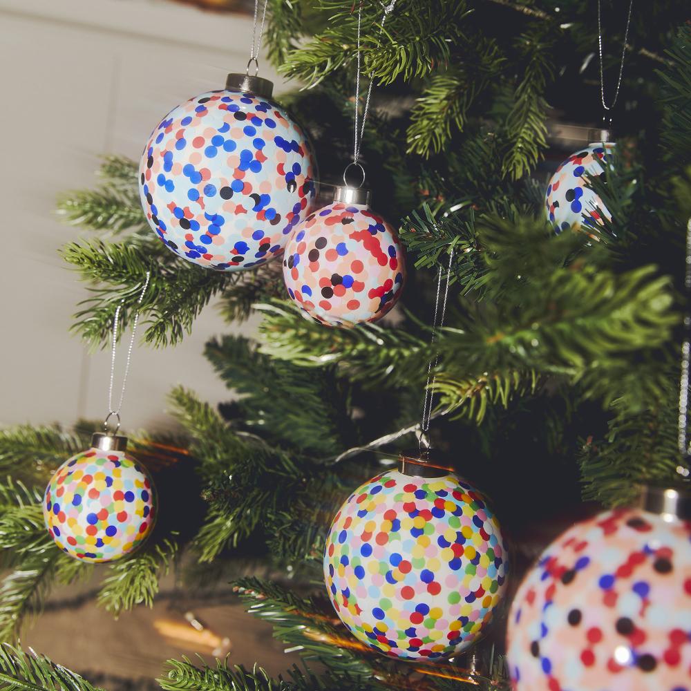Mehrere Alessi Proust Weihnachtskugeln mit bunten Punkten hängen an einem geschmückten Weihnachtsbaum.