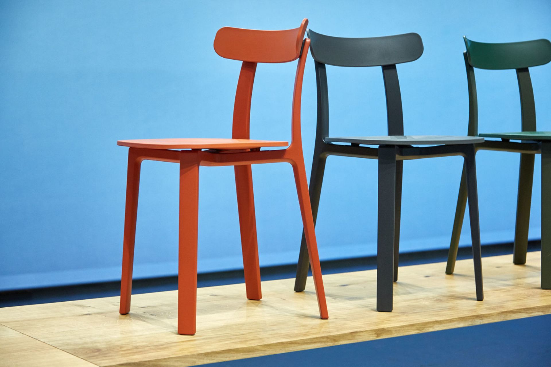 Vitra All Plastic Chair Outdoor Stuhl in Orange, Grau und Grün vor blauem Hintergrund.