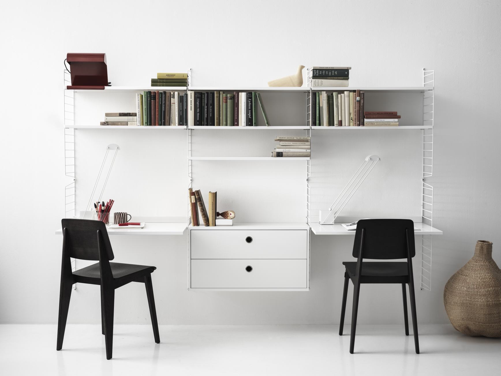 Weißes String Furniture Regalsystem mit zwei Schreibtischen und schwarzen Stühlen, Bücher und Dekoration für das Arbeitszimmer.