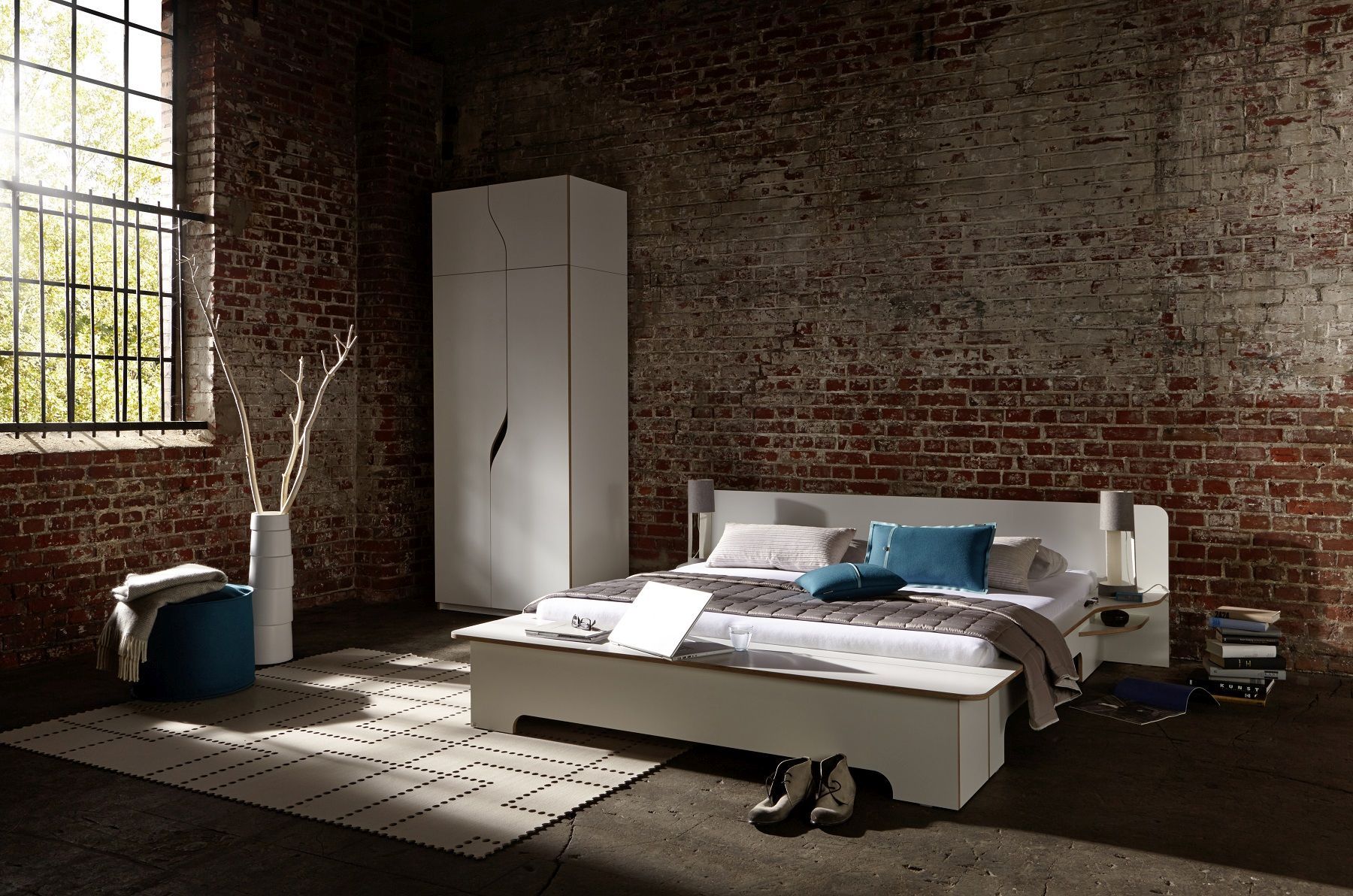 Modernes Plane Doppelbett von Müller Möbelwerkstätten in Loft-Atmosphäre mit Backsteinwand und weißen Möbeln.