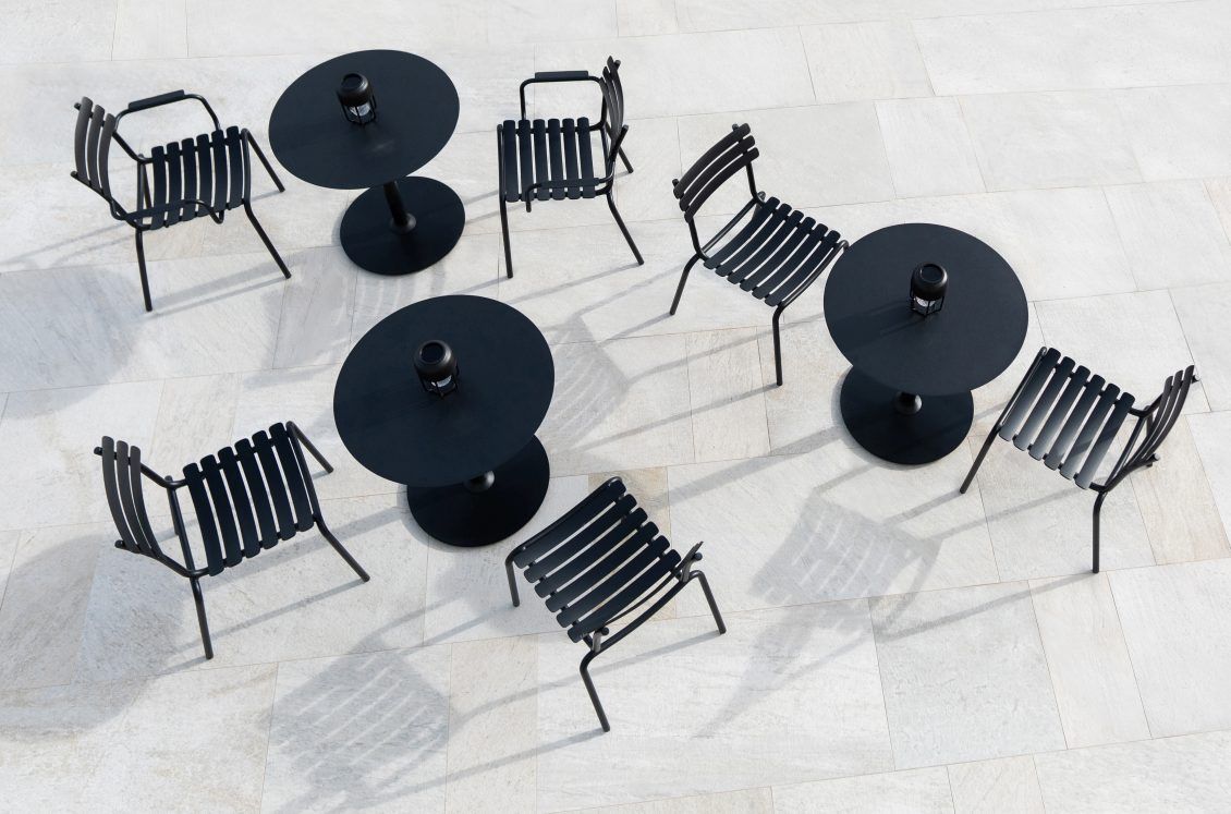 Draufsicht: Mehrere Alua Dining Stühle von Houe mit schwarzen Outdoor-Tischen auf heller Terrasse.