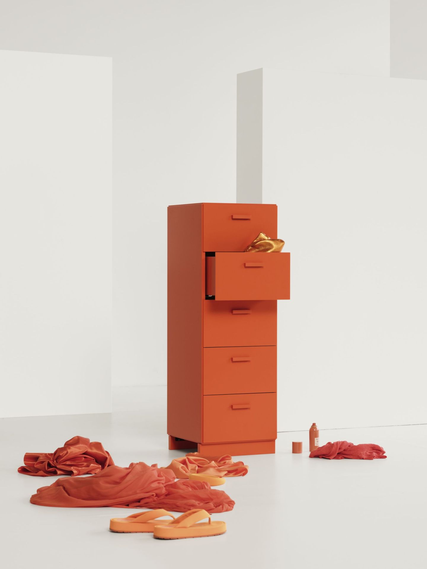 Orangefarbene Relief Kommode von String Furniture mit Sockel, Schublade geöffnet, Kleidung und Accessoires.