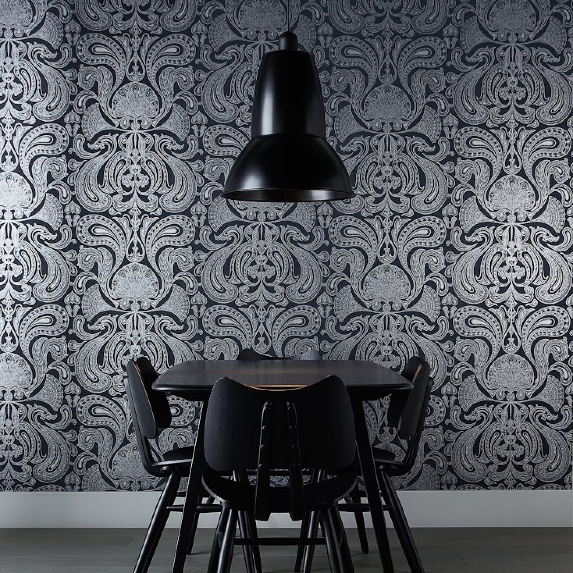 Schwarze Anglepoise Original 1227 Giant Pendelleuchte über Esstisch mit Stühlen vor gemusterter Tapete.