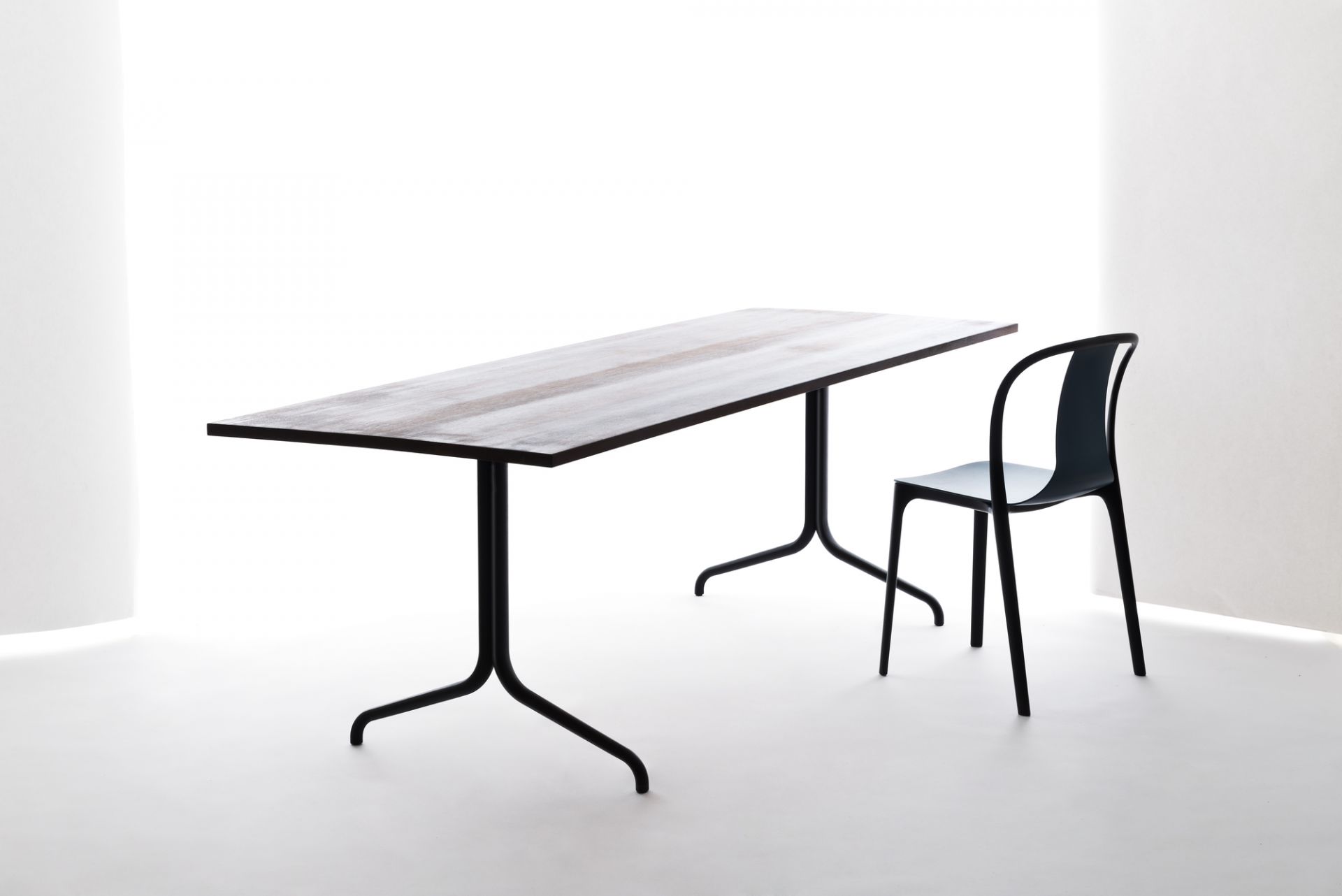 Vitra Belleville Chair Plastic Stuhl in Schwarz neben einem Esstisch mit dunkler Tischplatte.