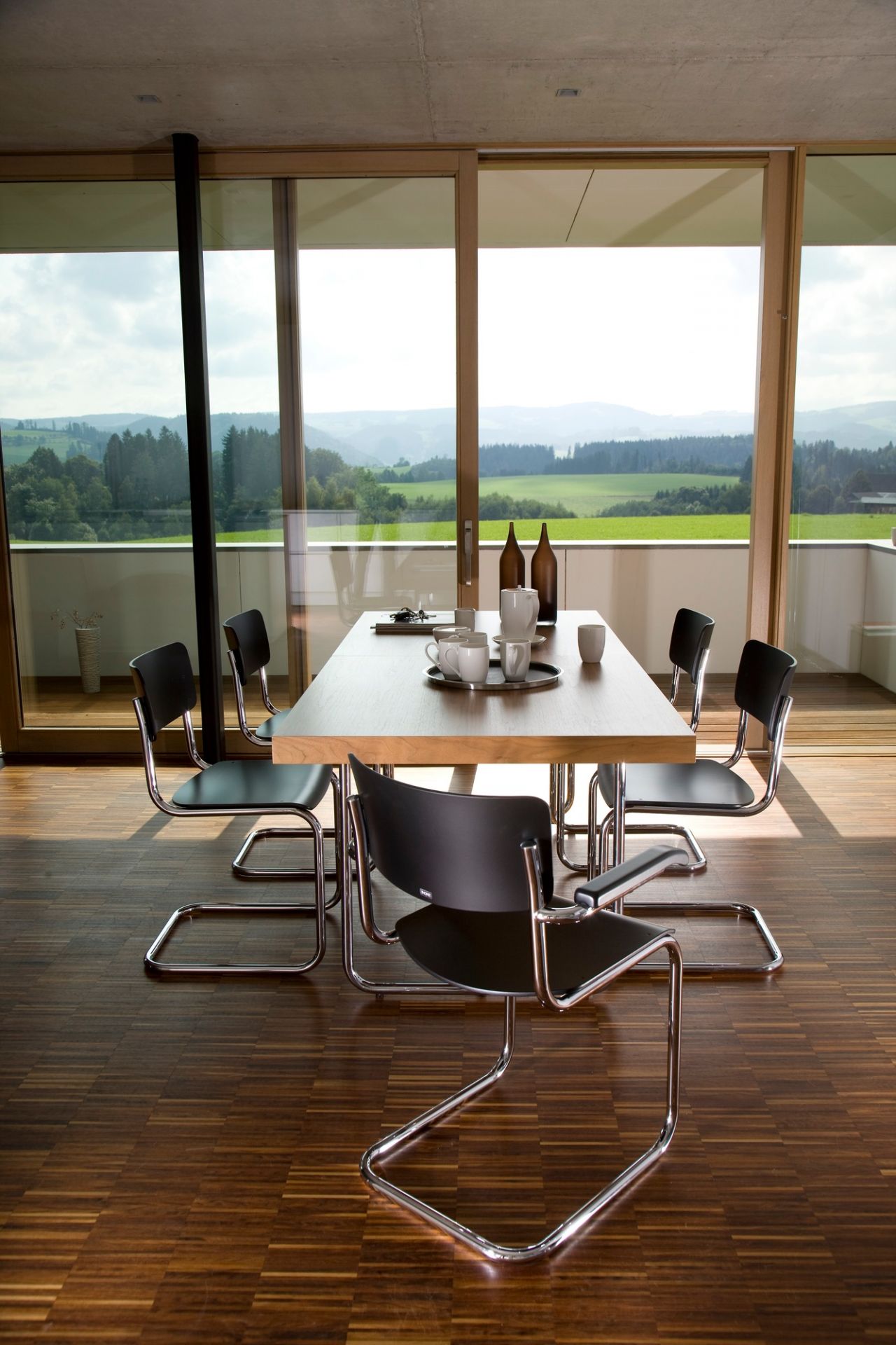 Esszimmer mit Thonet S 43 Stahlrohr Freischwinger Stühlen und Holztisch vor Panoramafenster mit Landschaftsblick.
