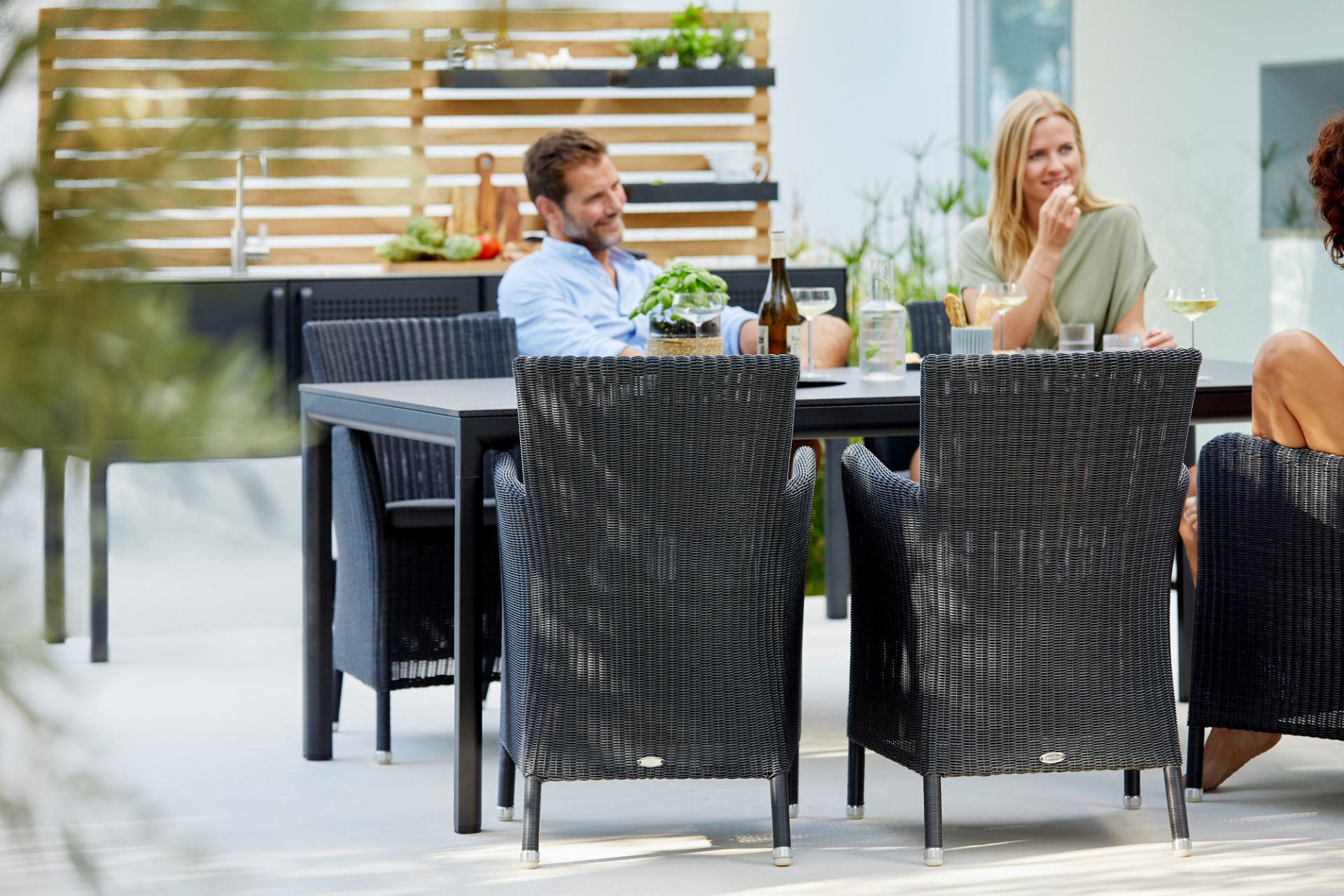 Cane-Line Hampsted Outdoor Sessel aus Rattan mit Esstisch und entspannten Personen im Garten.