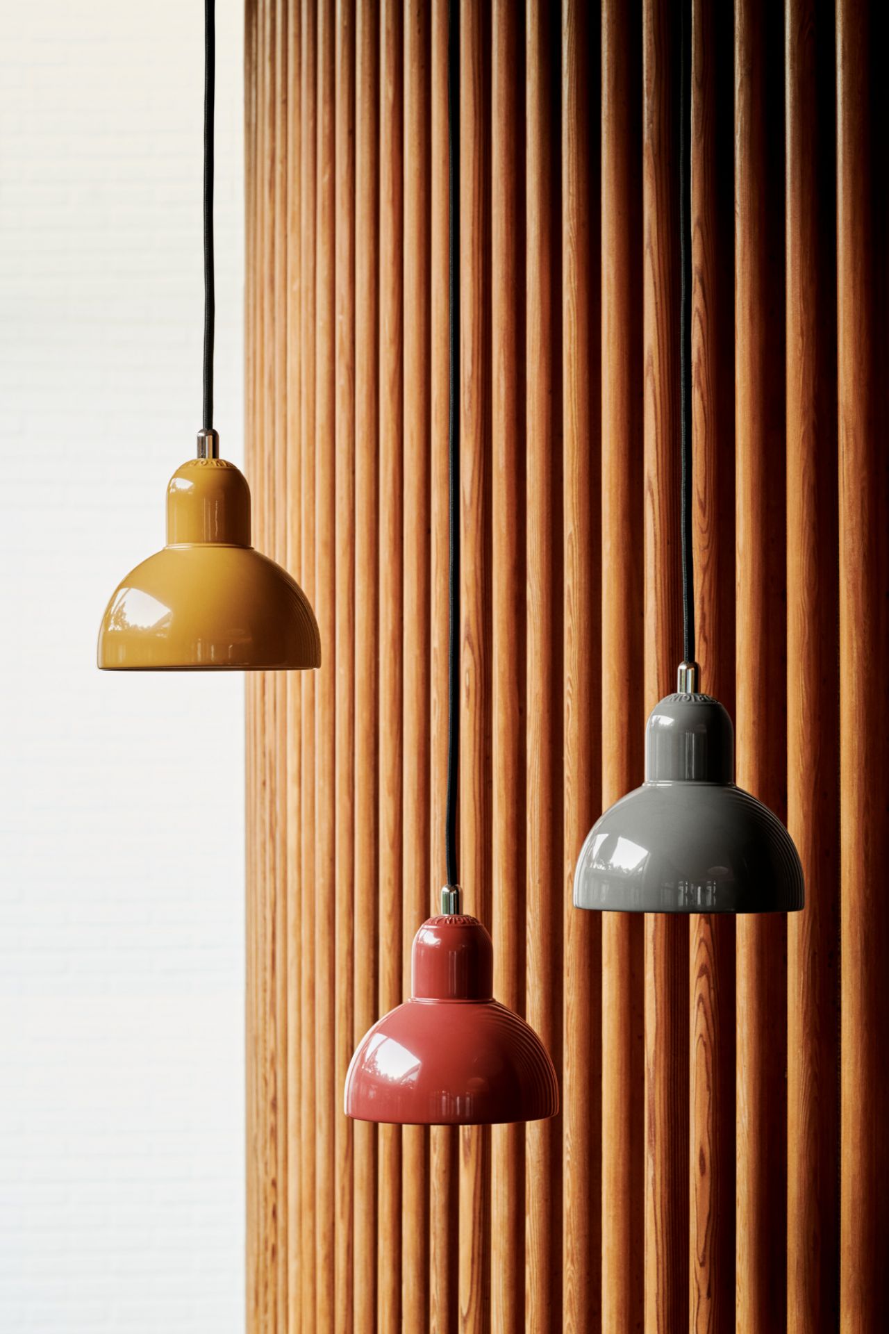 Drei Fritz Hansen Pendelleuchten 6722-P in Gelb, Rot und Grau vor Holzwand.