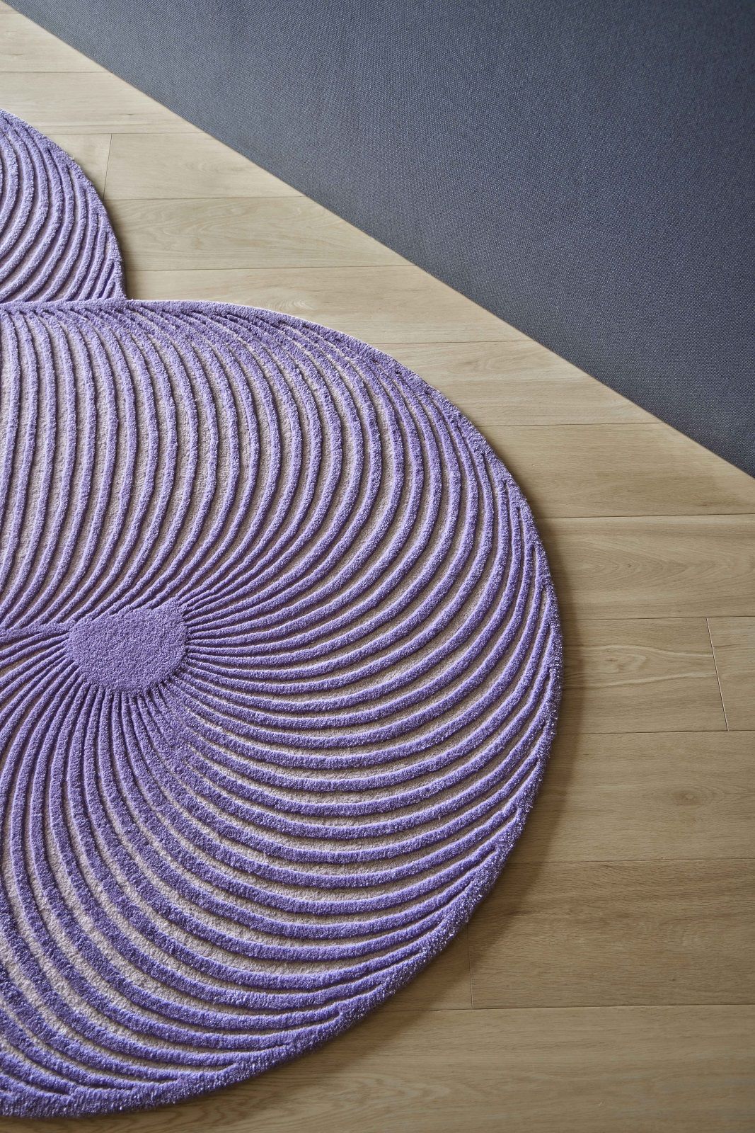 Detailaufnahme des lila Giro Teppichs von Gan mit konzentrischen Linien auf hellem Holzboden.