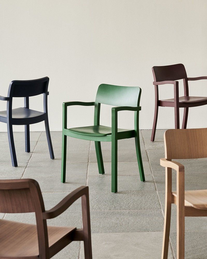 Verschiedenfarbige Armlehnstühle, darunter ein grüner Pastis Armchair von Hay, auf einem gefliesten Boden. Design Stühle für Esszimmer und Wohnbereich.