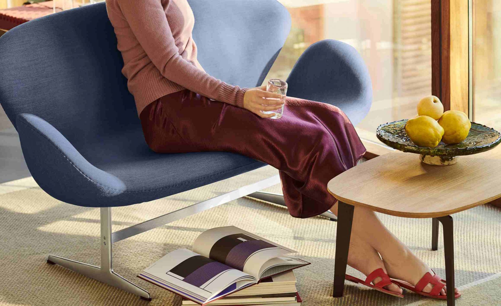 Frau sitzt entspannt im blauen Swan Chair von Fritz Hansen mit Wasserglas in der Hand.