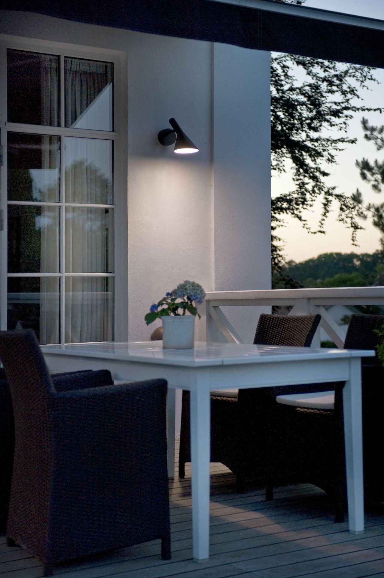 AJ 50 Wandleuchte von Louis Poulsen beleuchtet Terrasse mit Tisch und Stühlen im Außenbereich.