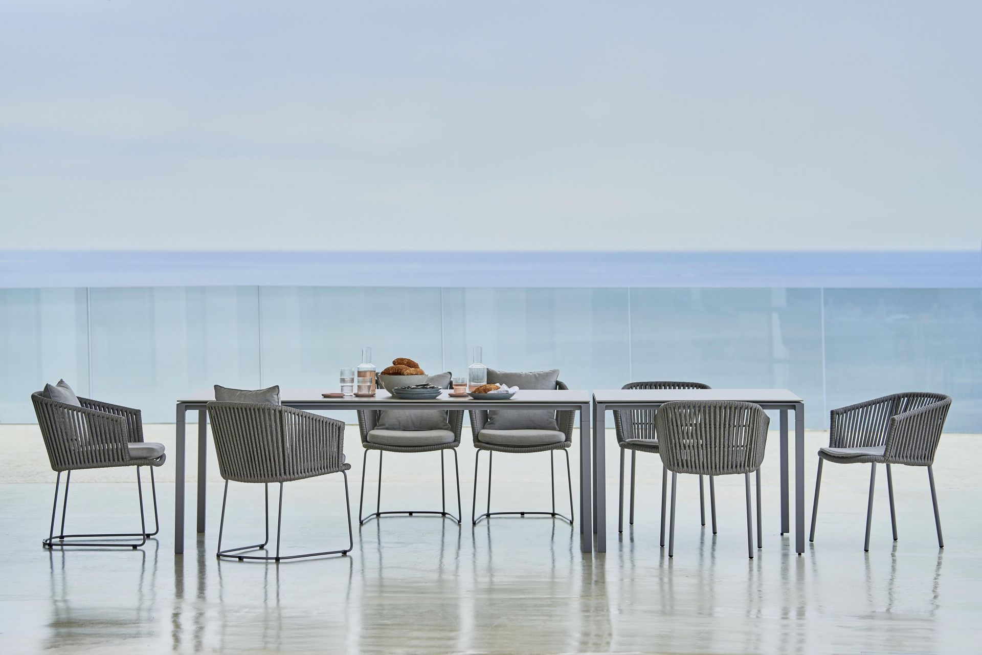 Pure Outdoor Esstisch von Cane-Line mit sechs Stühlen und grauem Seilgeflecht vor Meerblick.