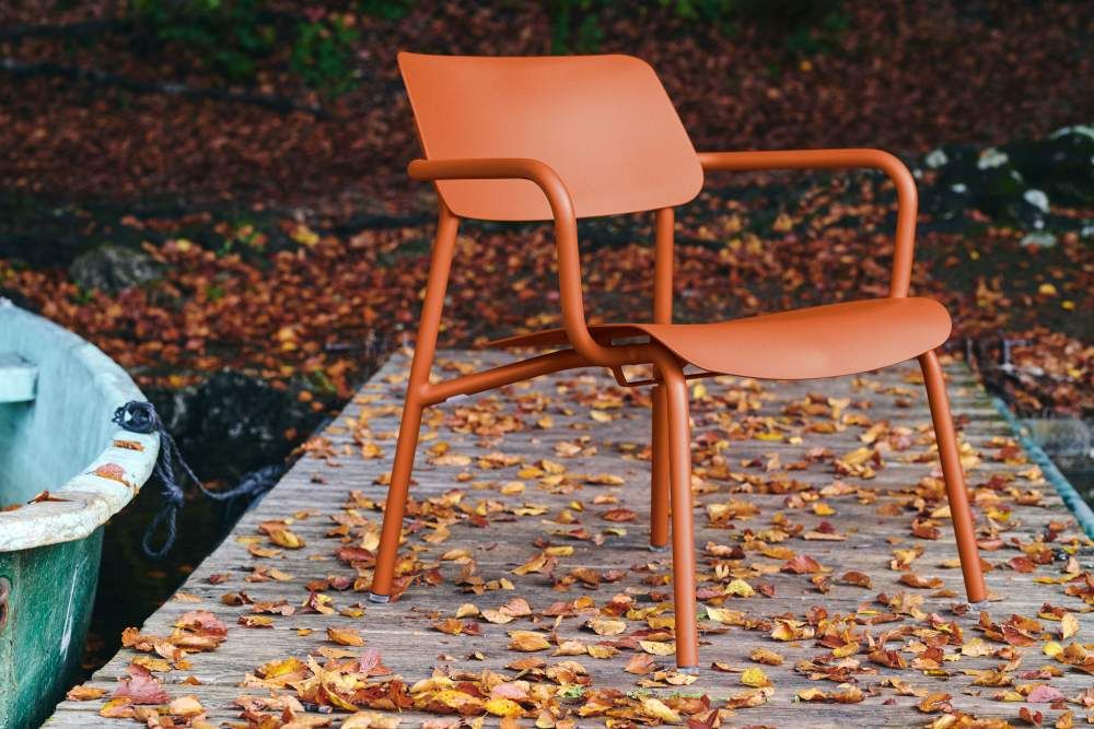 Orangefarbener Fermob Studie Lounge Sessel für den Außenbereich auf einem Holzsteg mit Herbstlaub.