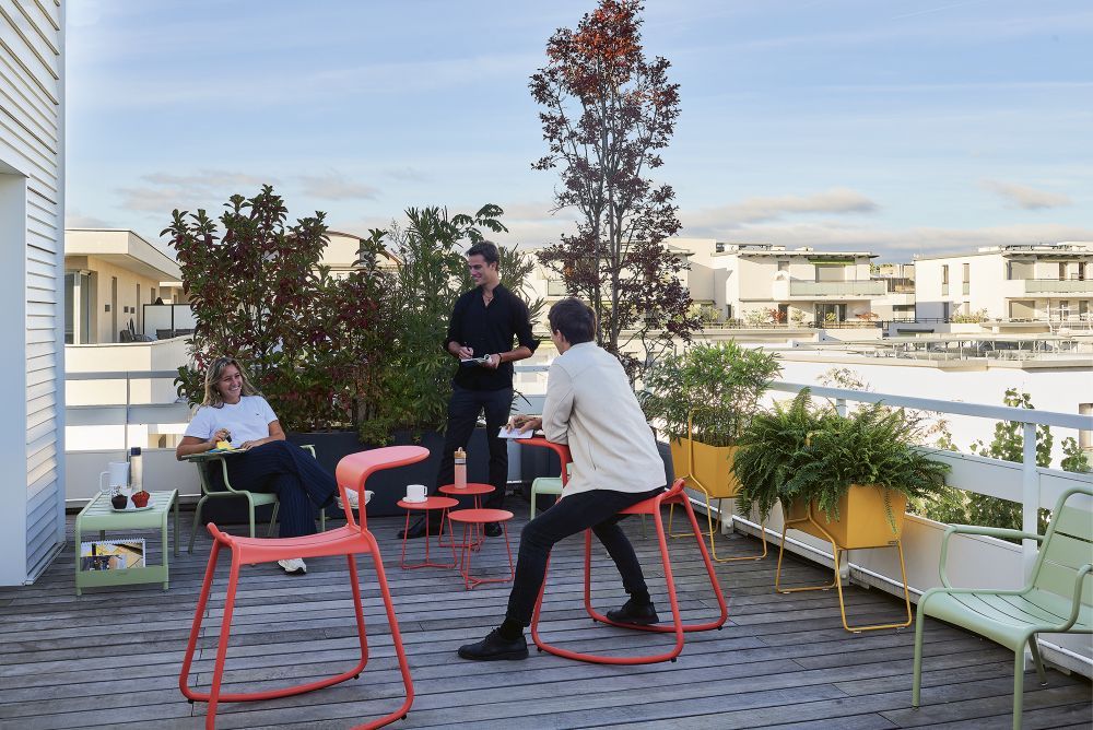 Adadesk Beistelltisch und Fermob Wippe Outdoor Möbel auf einer Dachterrasse mit Personen.