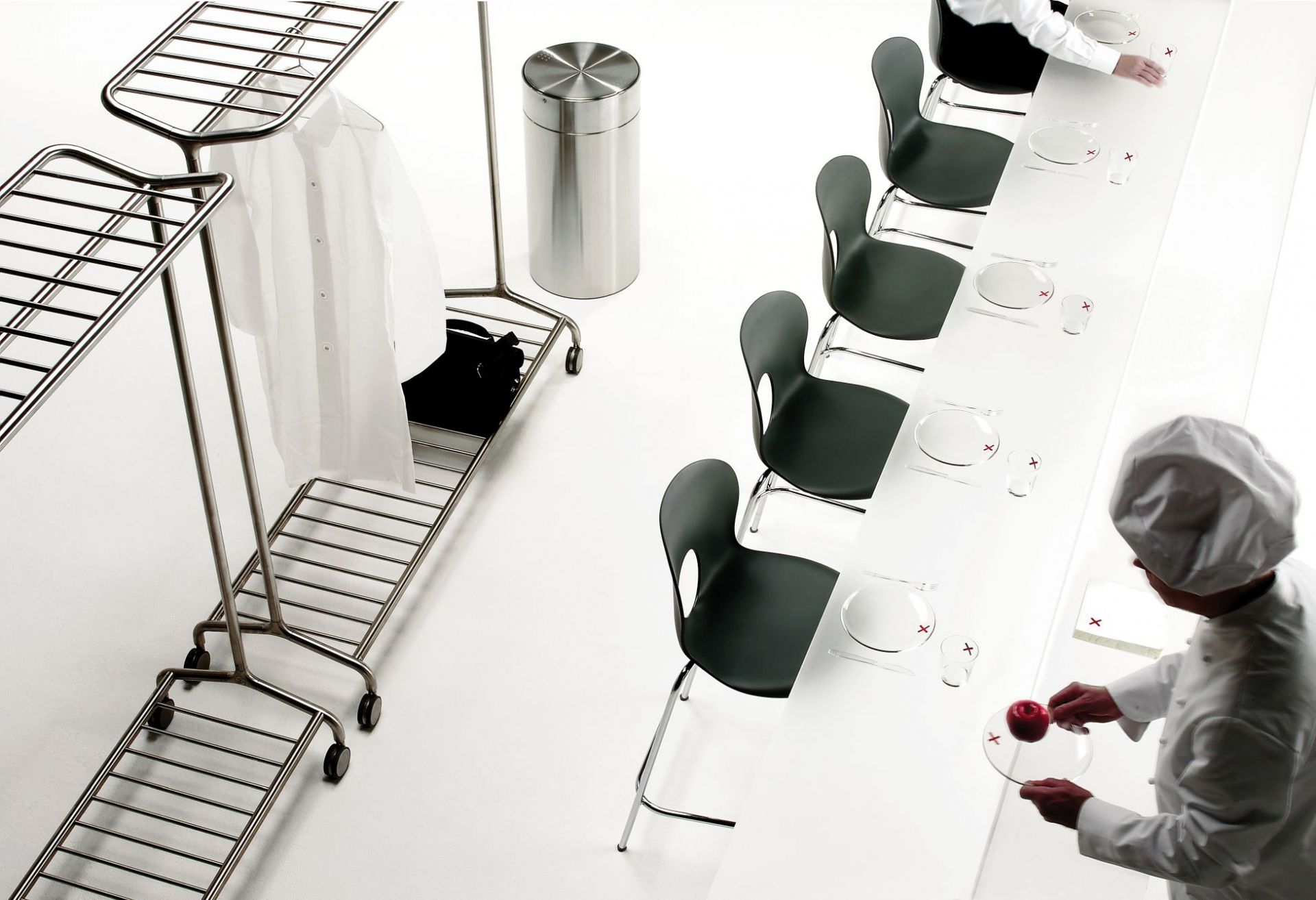 Edelstahl Papierkorb NOX von Rexite neben Kleiderständer und gedecktem Tisch in minimalistischem Design.