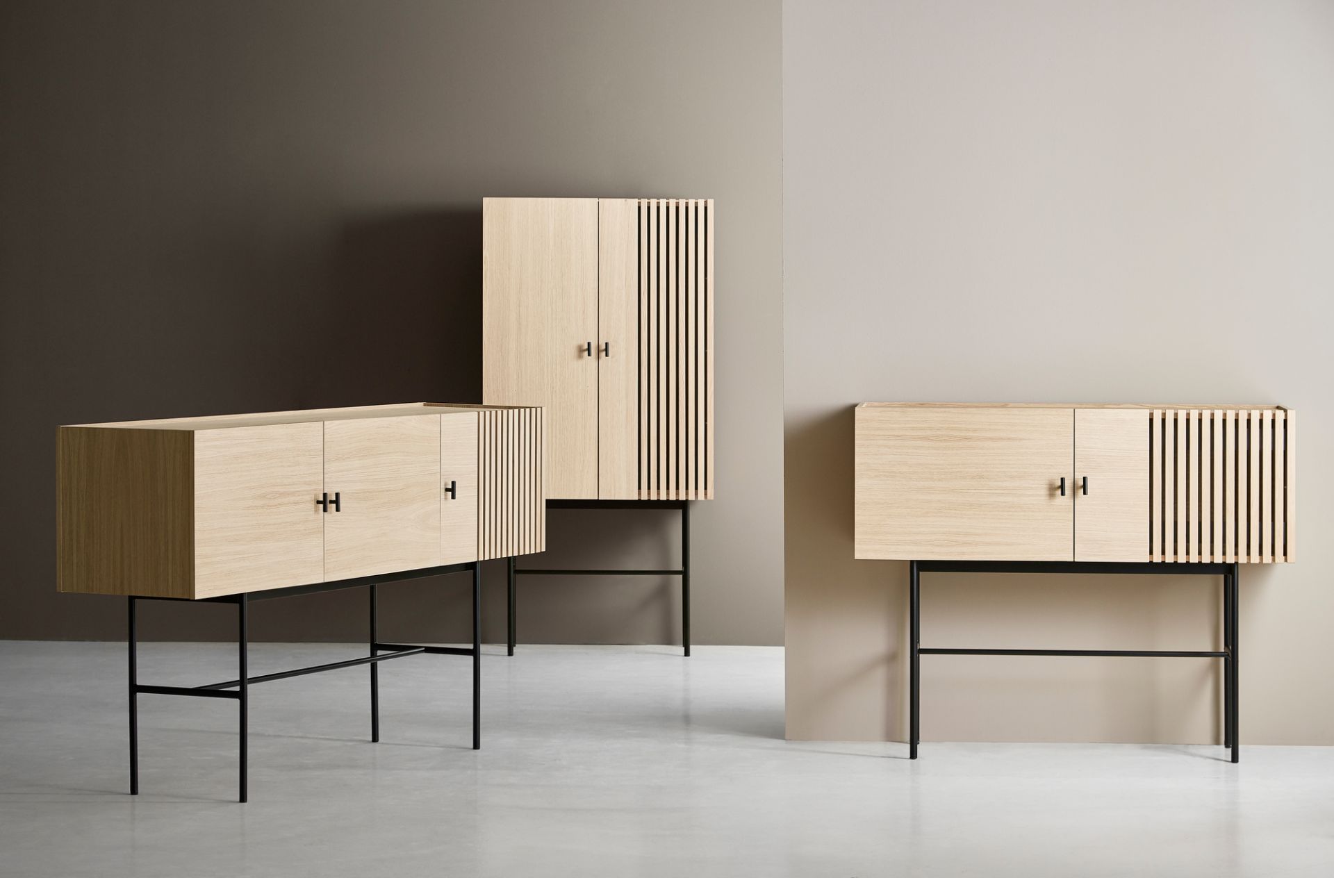 Array Highboard Eiche von Woud: Drei moderne Schränke aus hellem Eichenholz mit schwarzen Metallbeinen.
