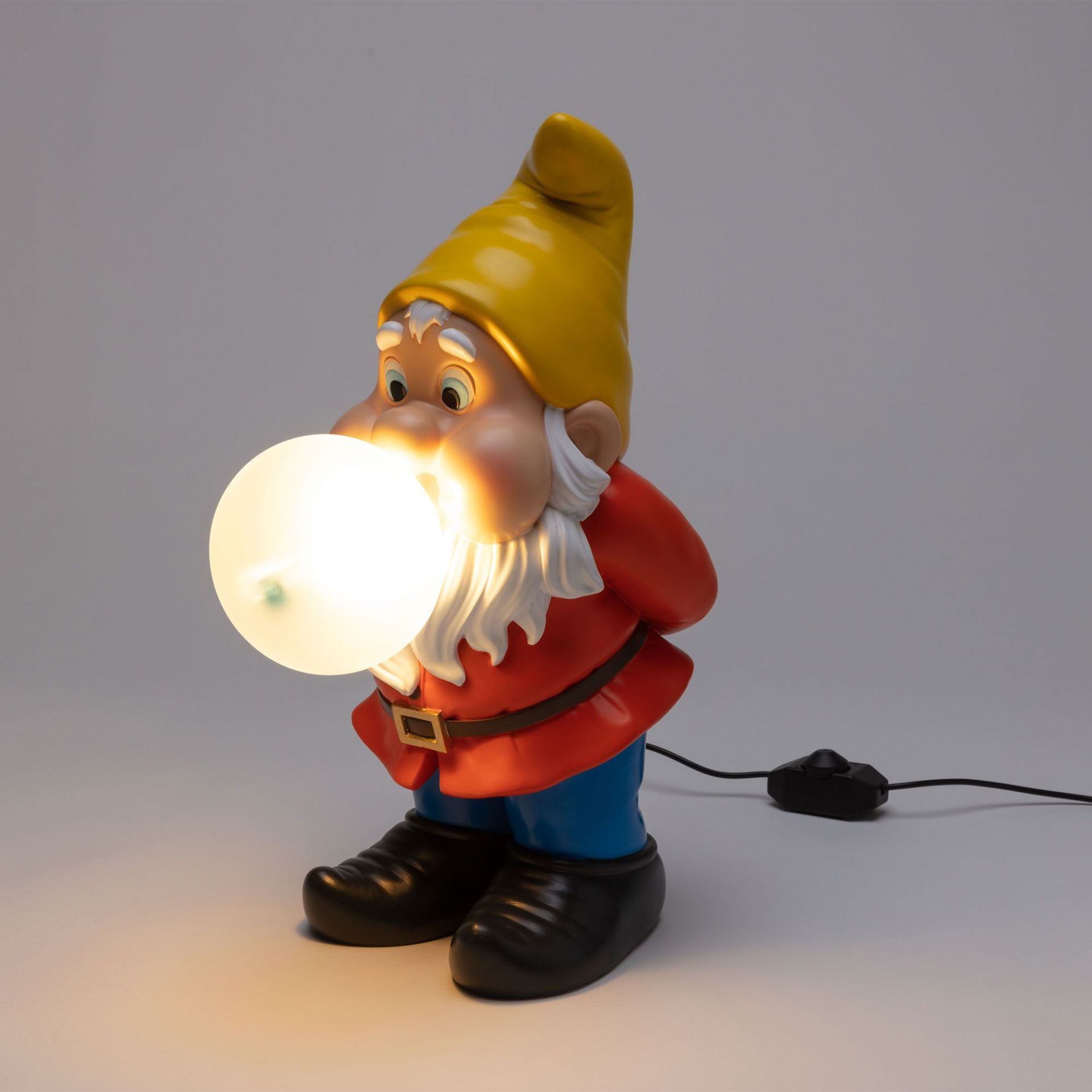 Seletti Gummy Snooping Lampe: Gartenzwerg Figur mit gelbem Hut und leuchtender Kugel als Mund.