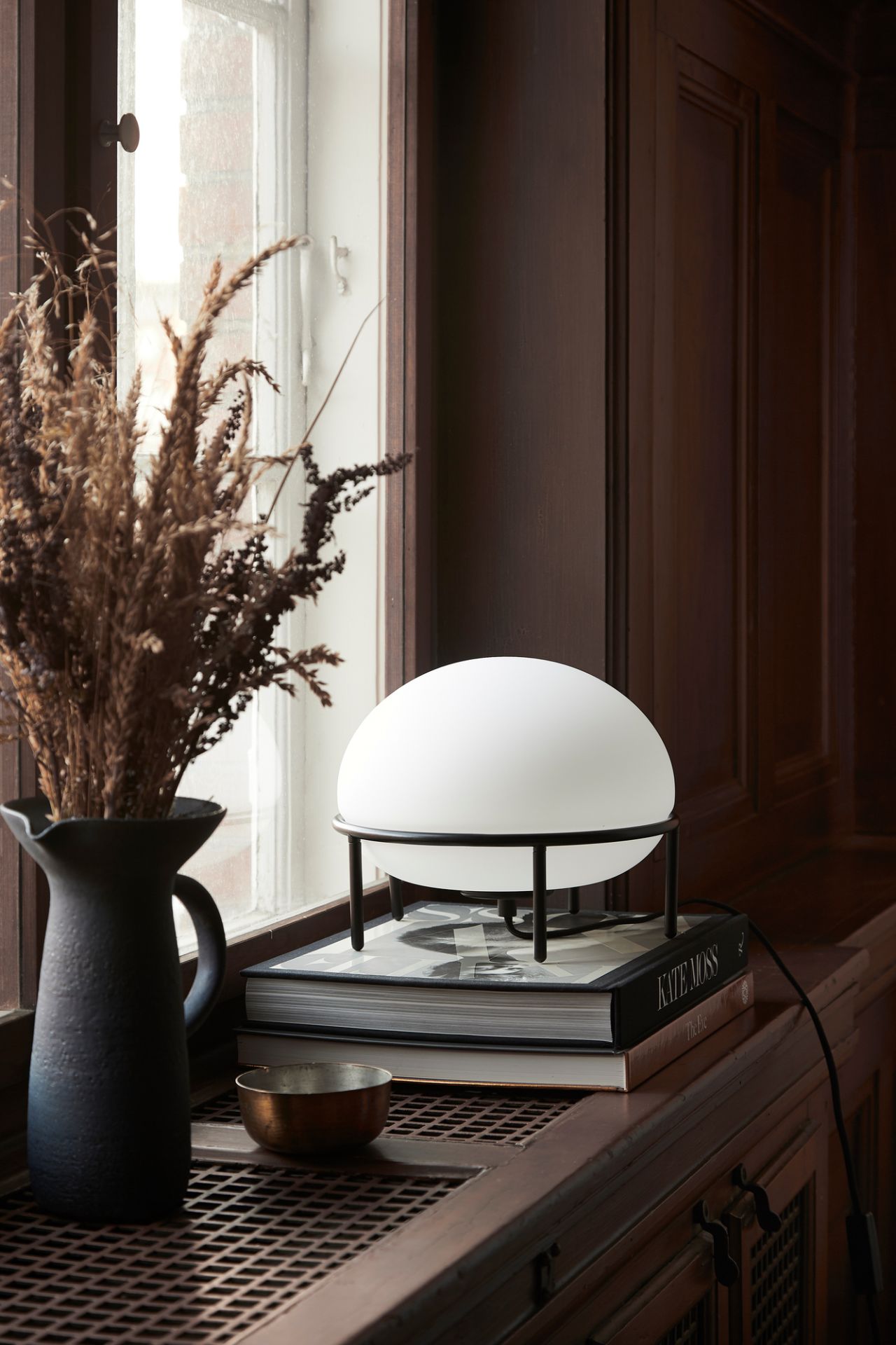 Woud Tischleuchte Pump Table Lamp: Runde, moderne Lampe mit schwarzem Gestell auf Büchern.
