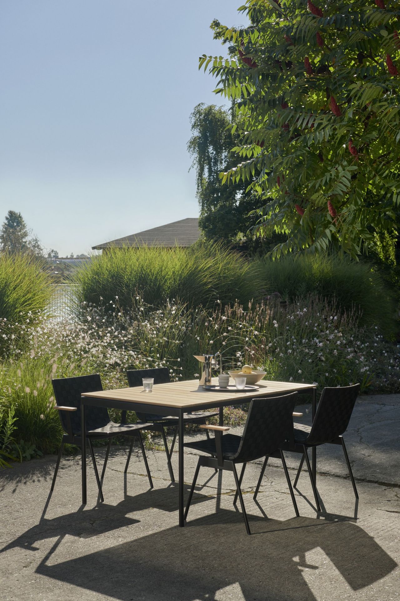 AndTradition Ville AV34 Outdoor Stuhl, schwarzes Design, mit Gartentisch und idyllischer Natur im Hintergrund.