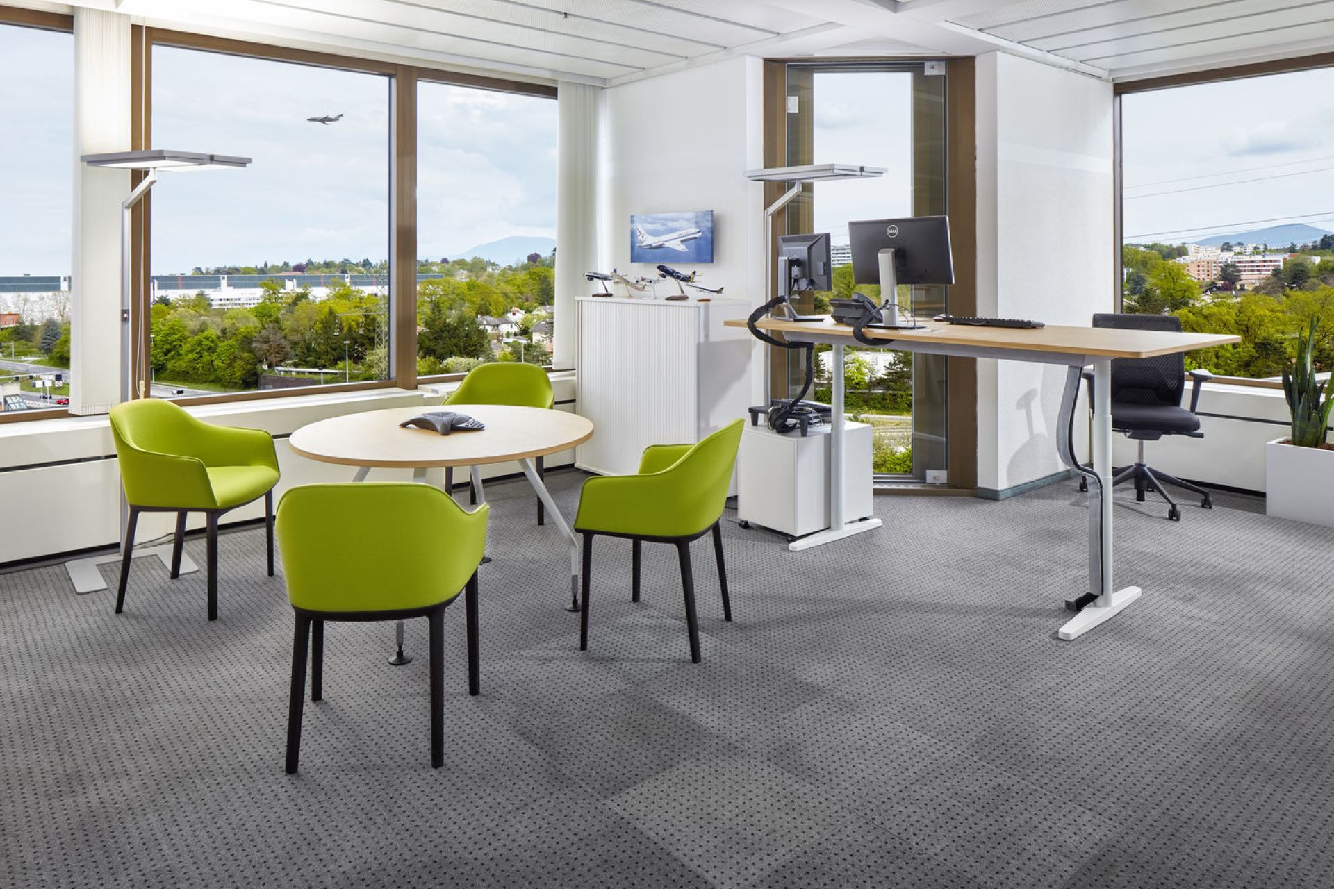 Büro mit Besprechungstisch und vier grünen Vitra Softshell Chairs mit Vierfußgestell vor großem Fenster.