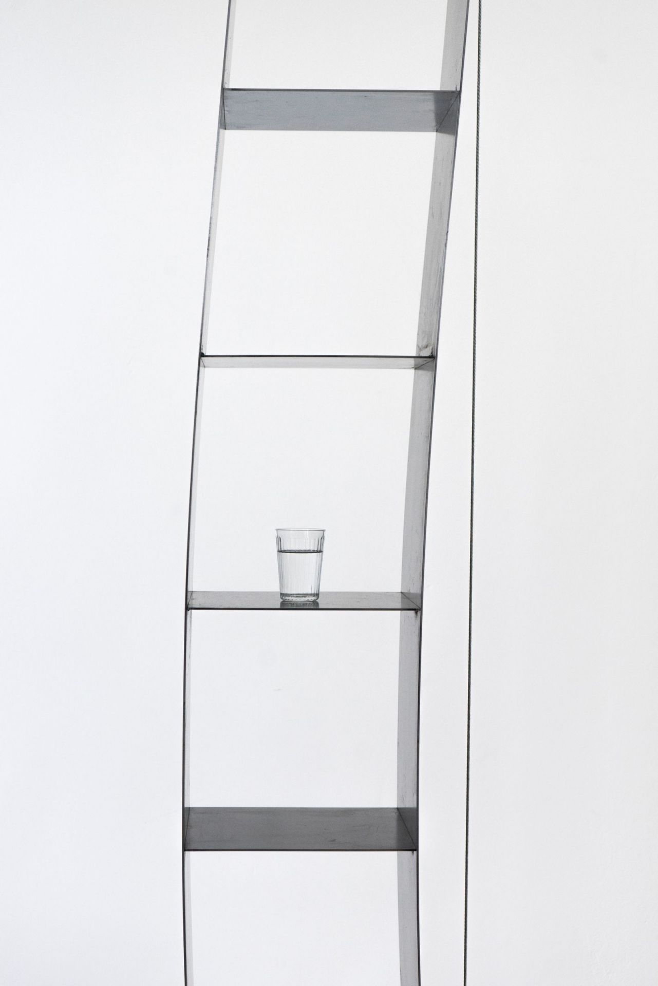 Nils Holger Moormann Gespanntes Regal vor weißer Wand mit Wasserglas auf einem der Regalböden.