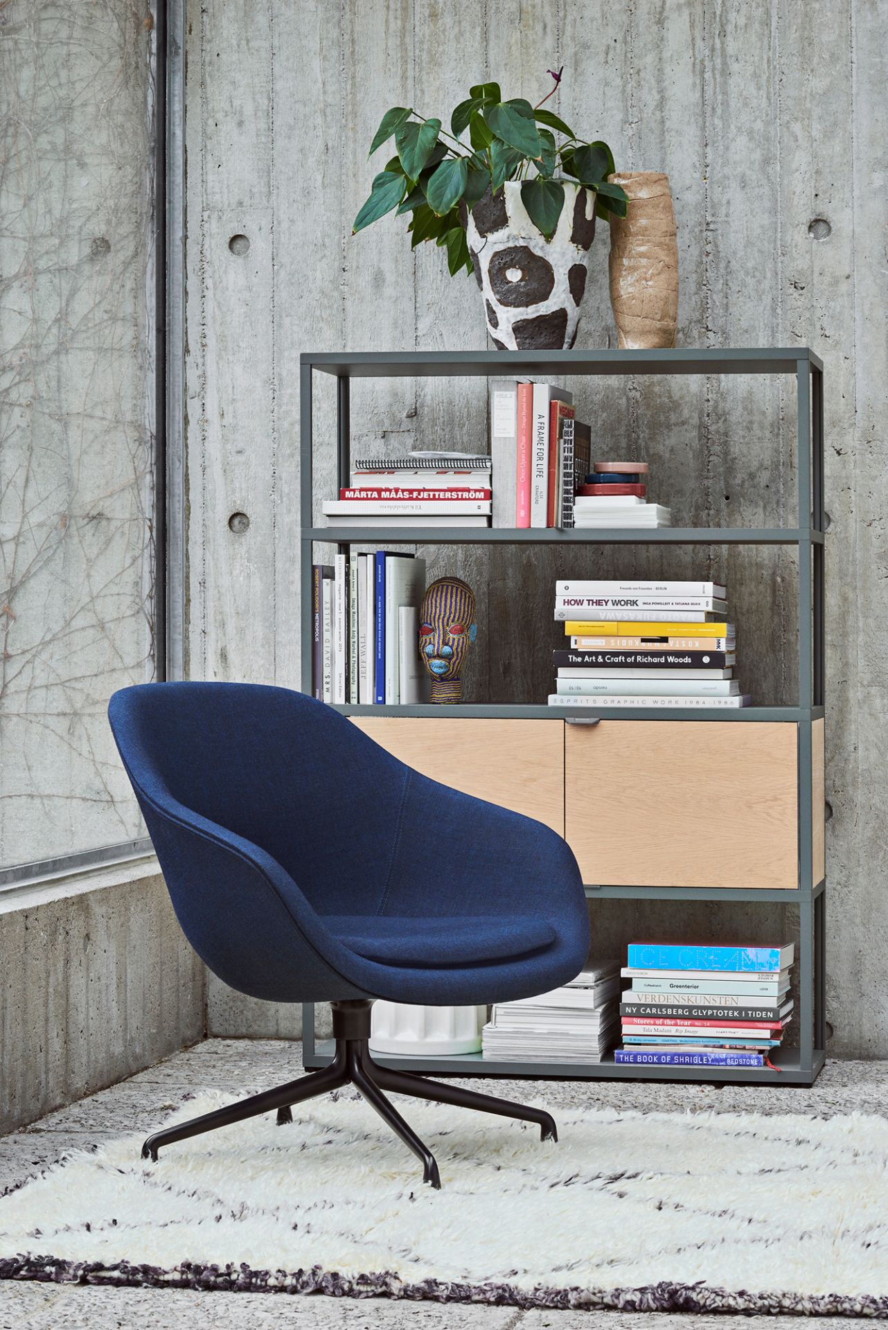 Blauer About a Lounge AAL 81 Drehsessel von Hay vor Bücherregal und Betonwand.