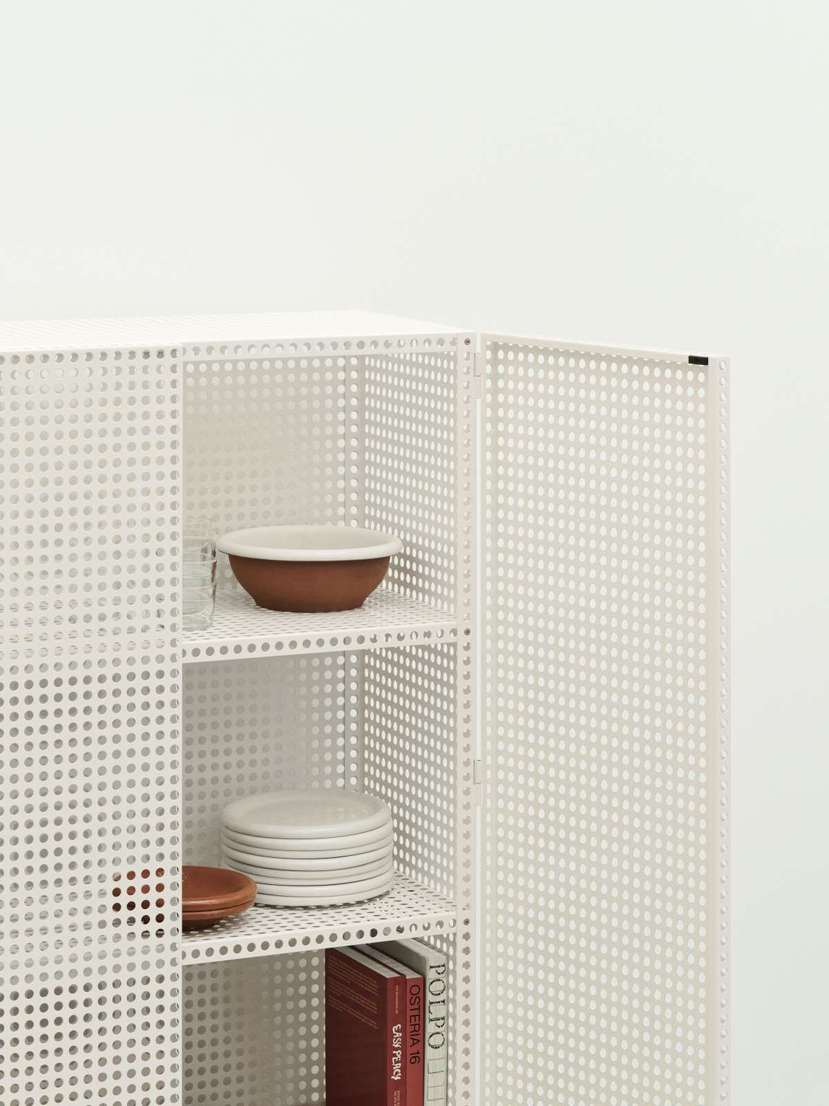 Weißes Hay Sideboard "Perforated Cabinet Floor Large" mit perforierter Metallstruktur und Geschirr auf den Regalen.