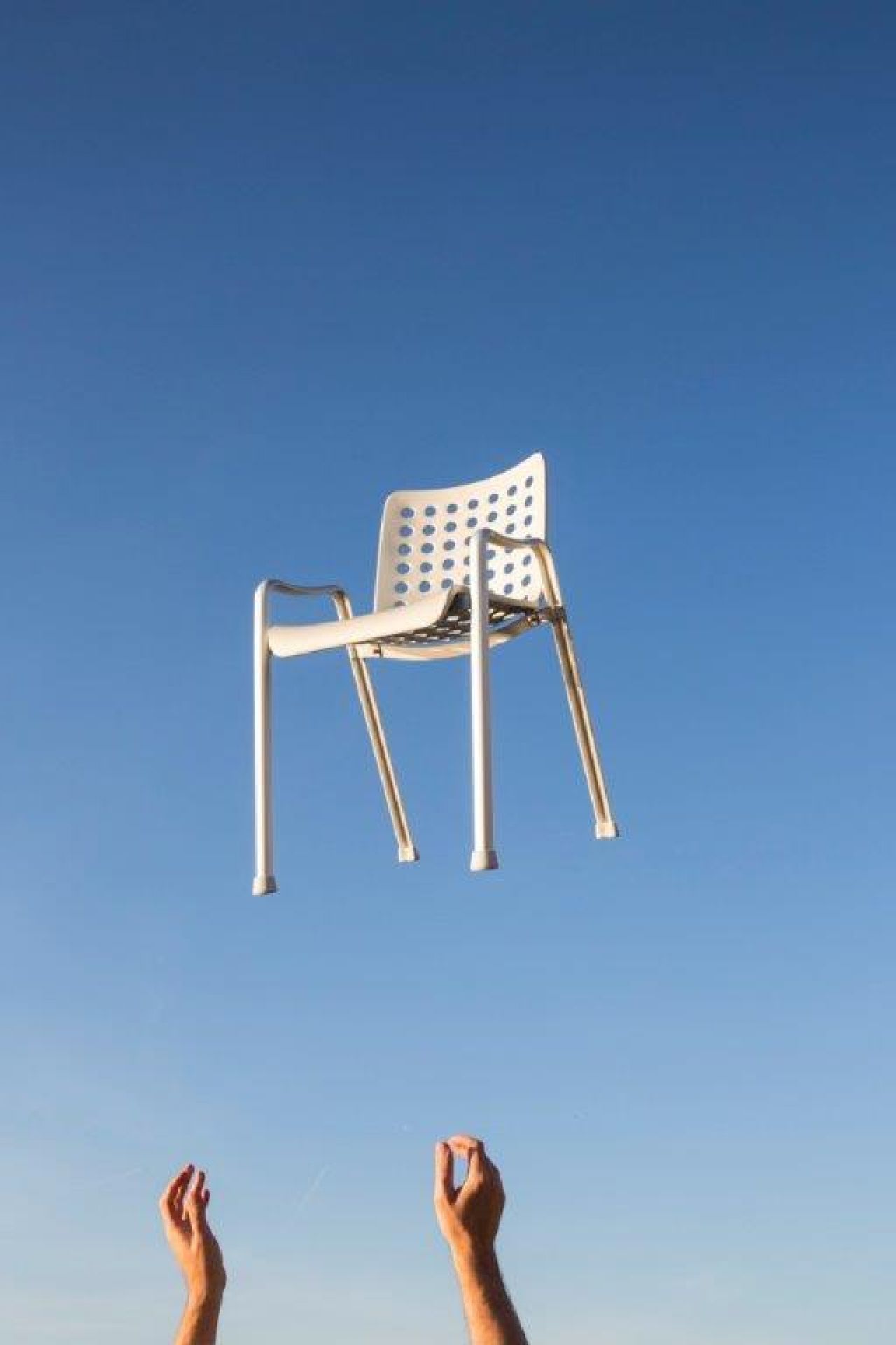Schweben des weißen Landi Stuhls von Vitra vor blauem Himmel, Hände im Vordergrund.