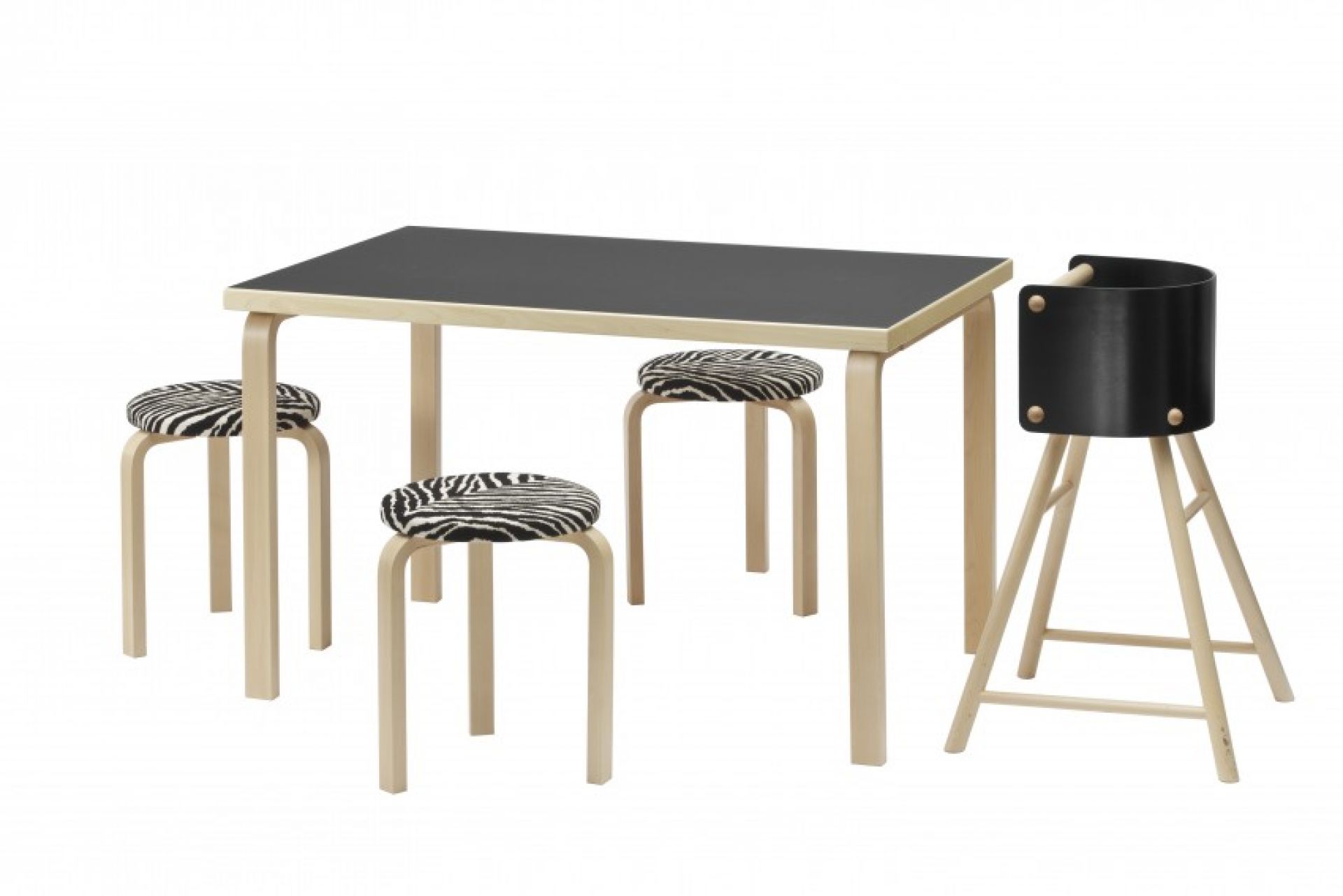 Artek 81B Tisch mit schwarzer Tischplatte, drei Zebra-gemusterten Hockern und einem Kinderhochstuhl aus Holz.