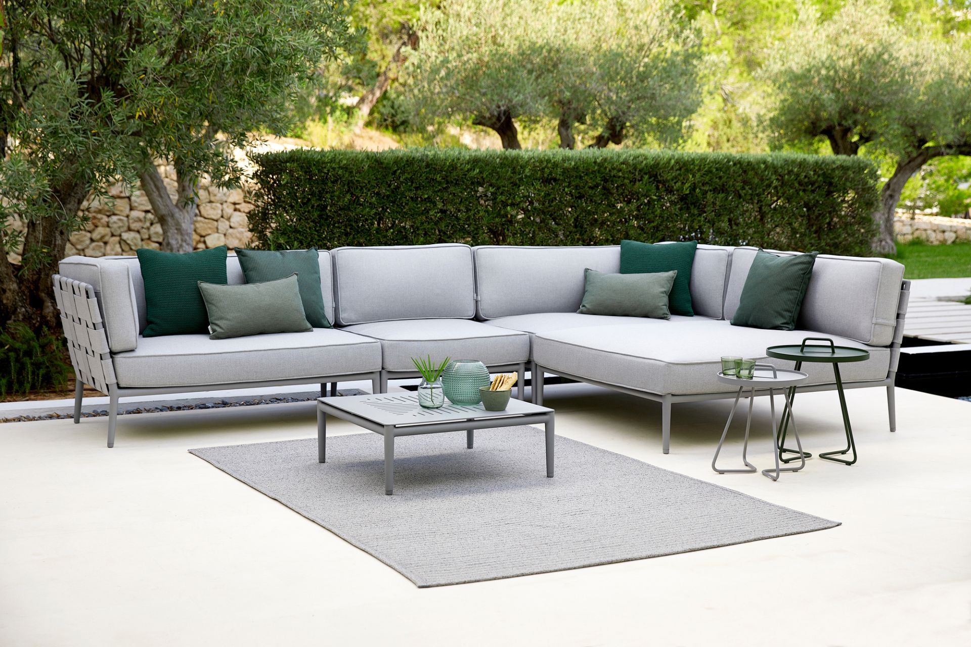 Conic AirTouch Modulsofa von Cane-Line, hellgraues Outdoor Sofa mit grünen Kissen und passendem Gartentisch.