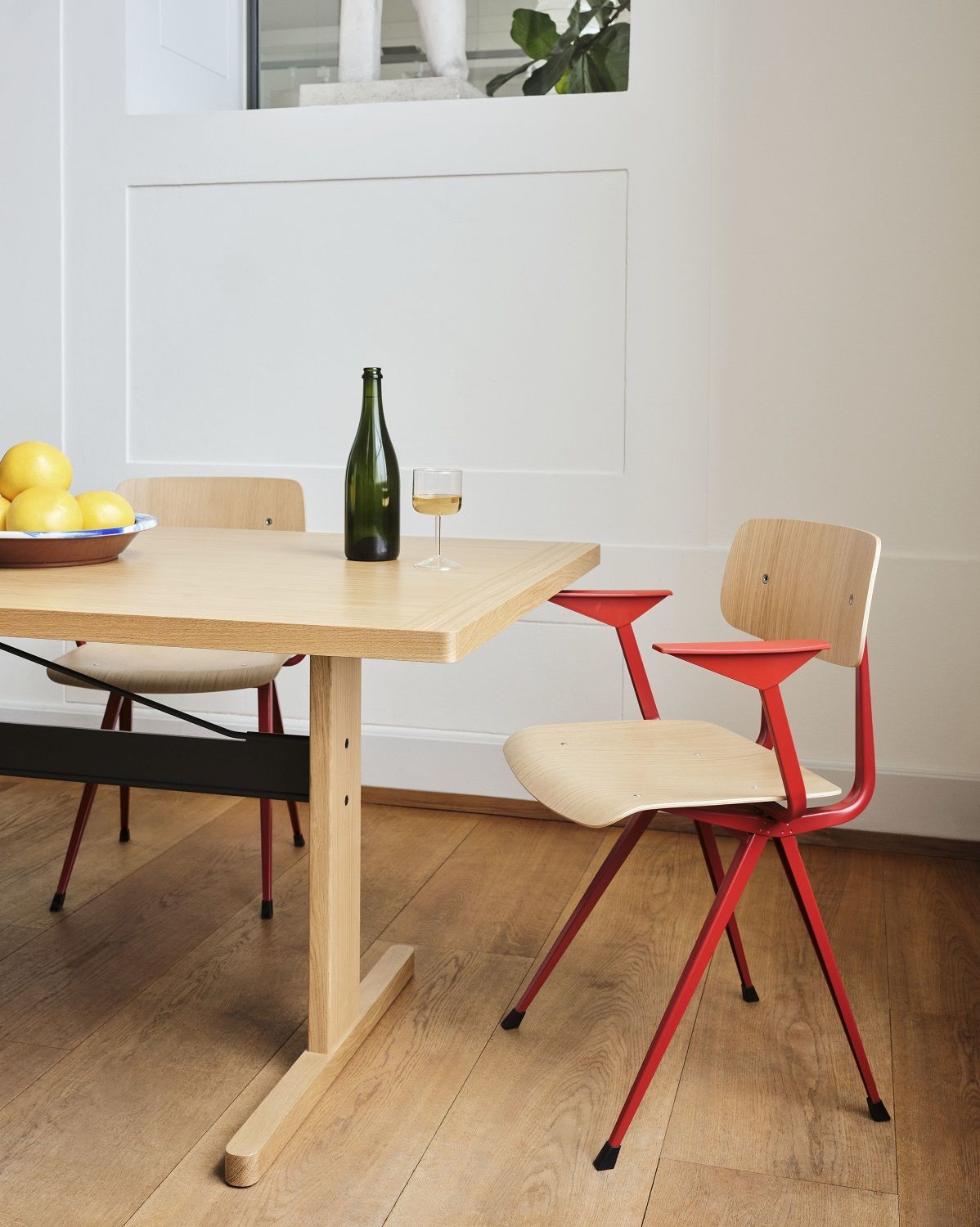 Heller Esstisch mit zwei Hay Result Armchair Stühlen, einer mit rotem Gestell, im minimalistischen Interieur.
