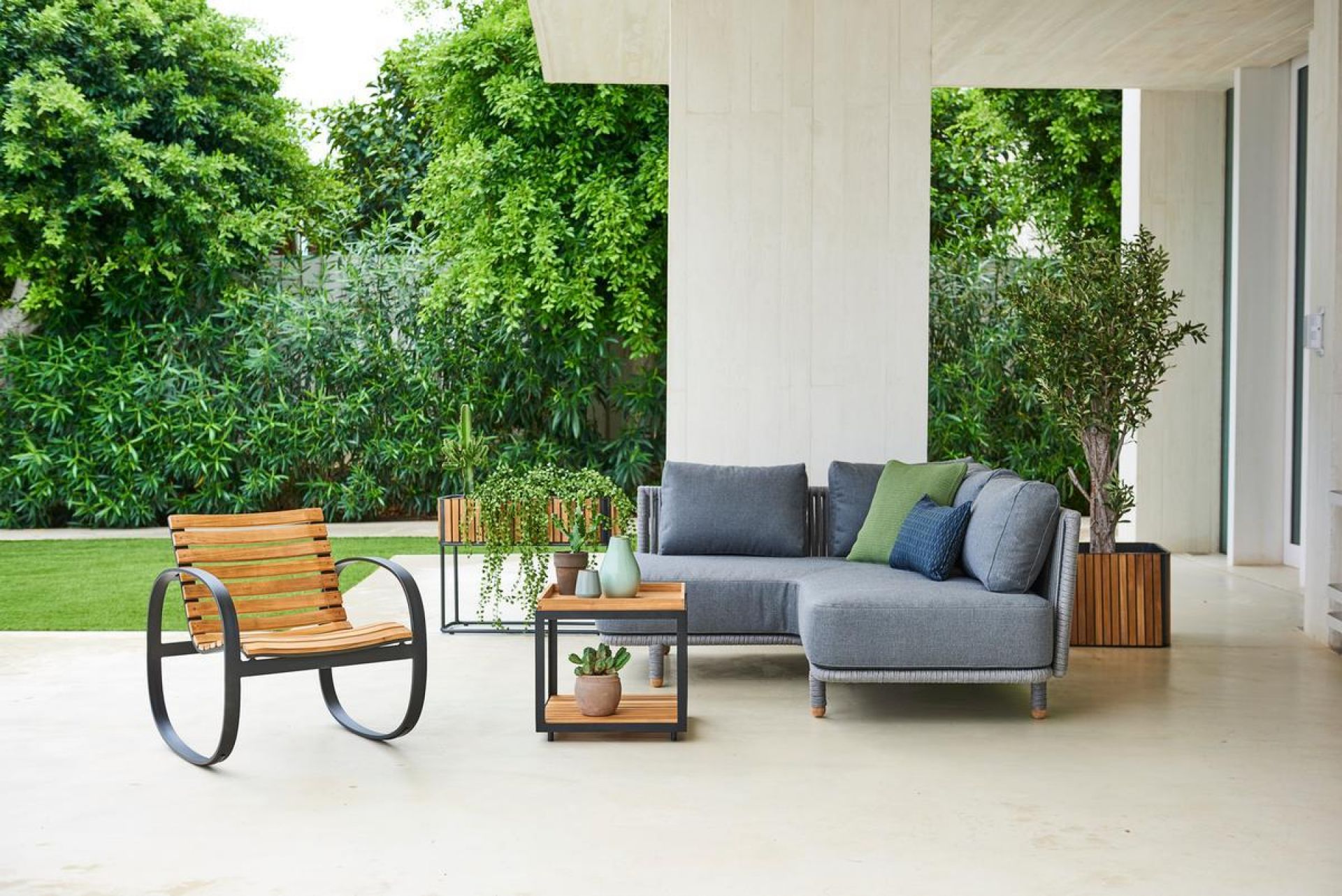 Cane-Line Moments Outdoor Sofa Eckmodul, graues Lounge Sofa mit Kissen und Beistelltisch im Garten.