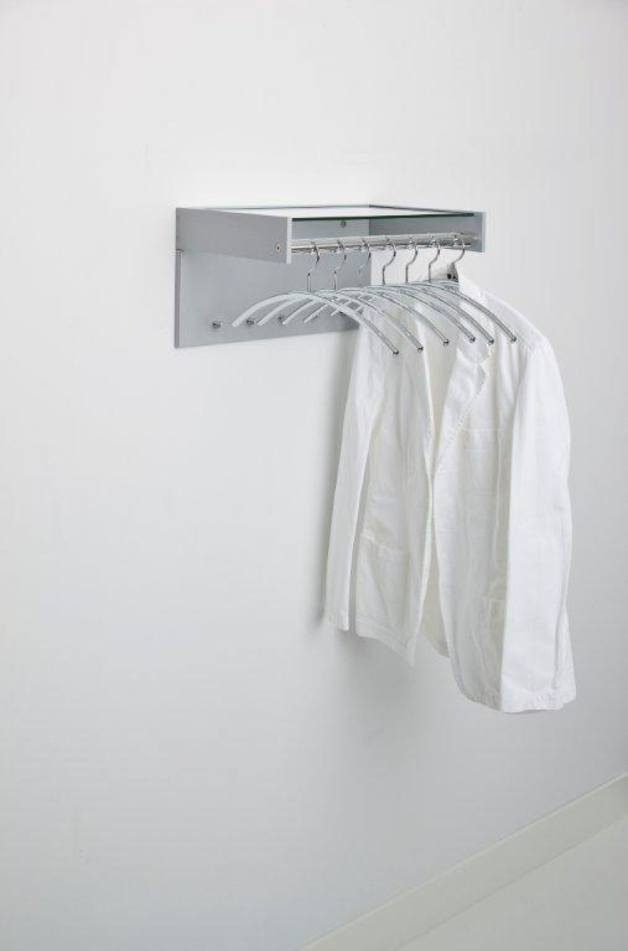 Hangon Wandgarderobe von Cascando mit Jacke an Chrom-Kleiderbügeln unter Ablage montiert an weißer Wand.