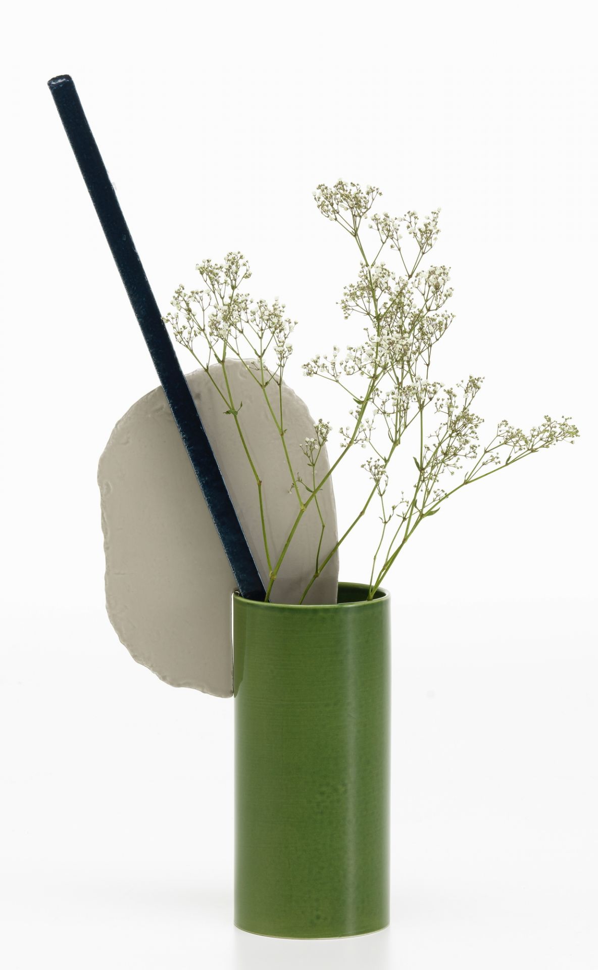 Grüne Vitra Découpage Vase mit Blumen, Stab und Keramikscheibe vor weißem Hintergrund.