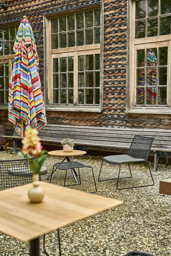 Weishäupl Slope Tisch Outdoor und Gartenmöbel-Set auf Kiesfläche vor rustikalem Gebäude.